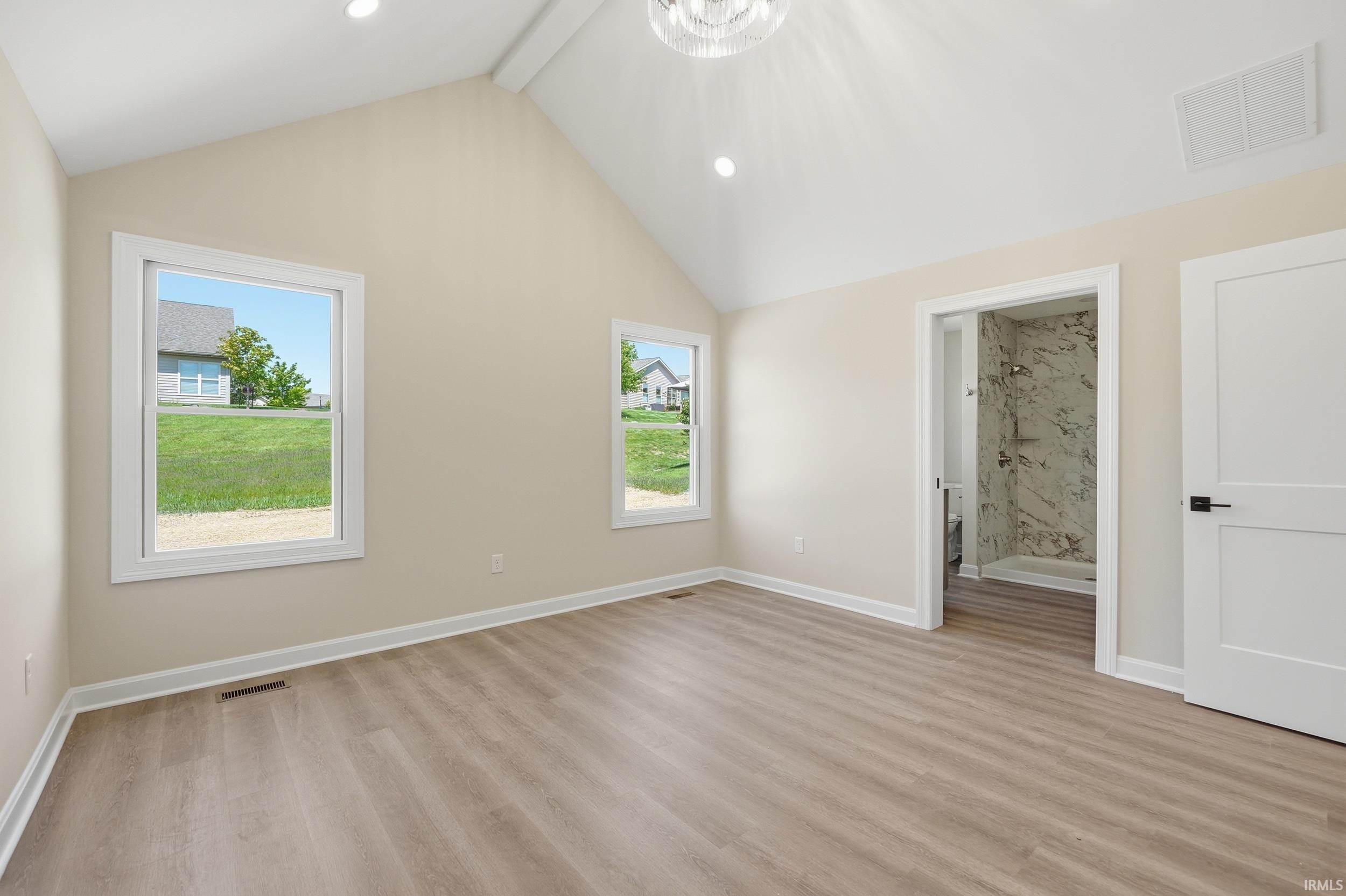 Spacious room featuring vaulted ceilings, recessed lighting, wood-finish flooring, and multiple windows for natural illumination