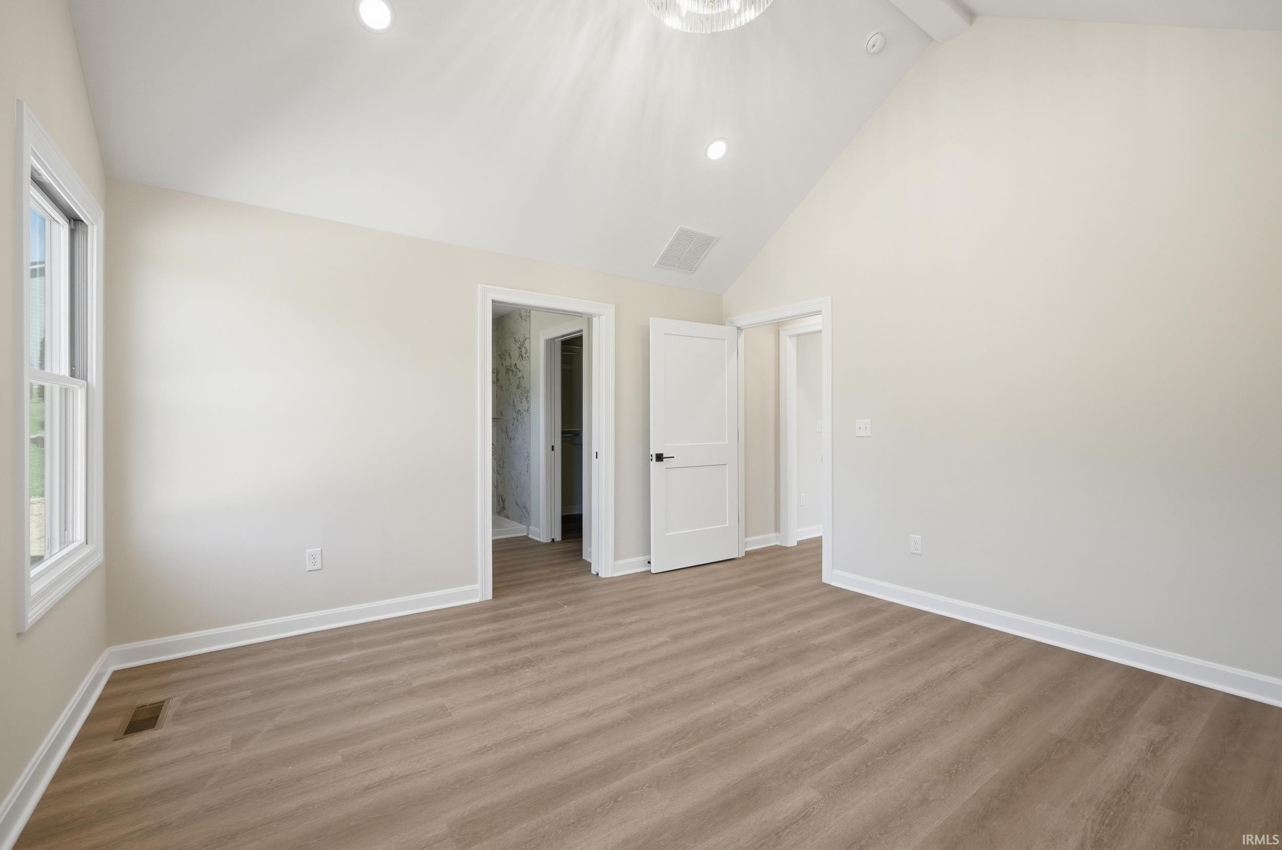 Spacious room featuring wood-finish flooring, vaulted ceiling with recessed lighting, and a white window