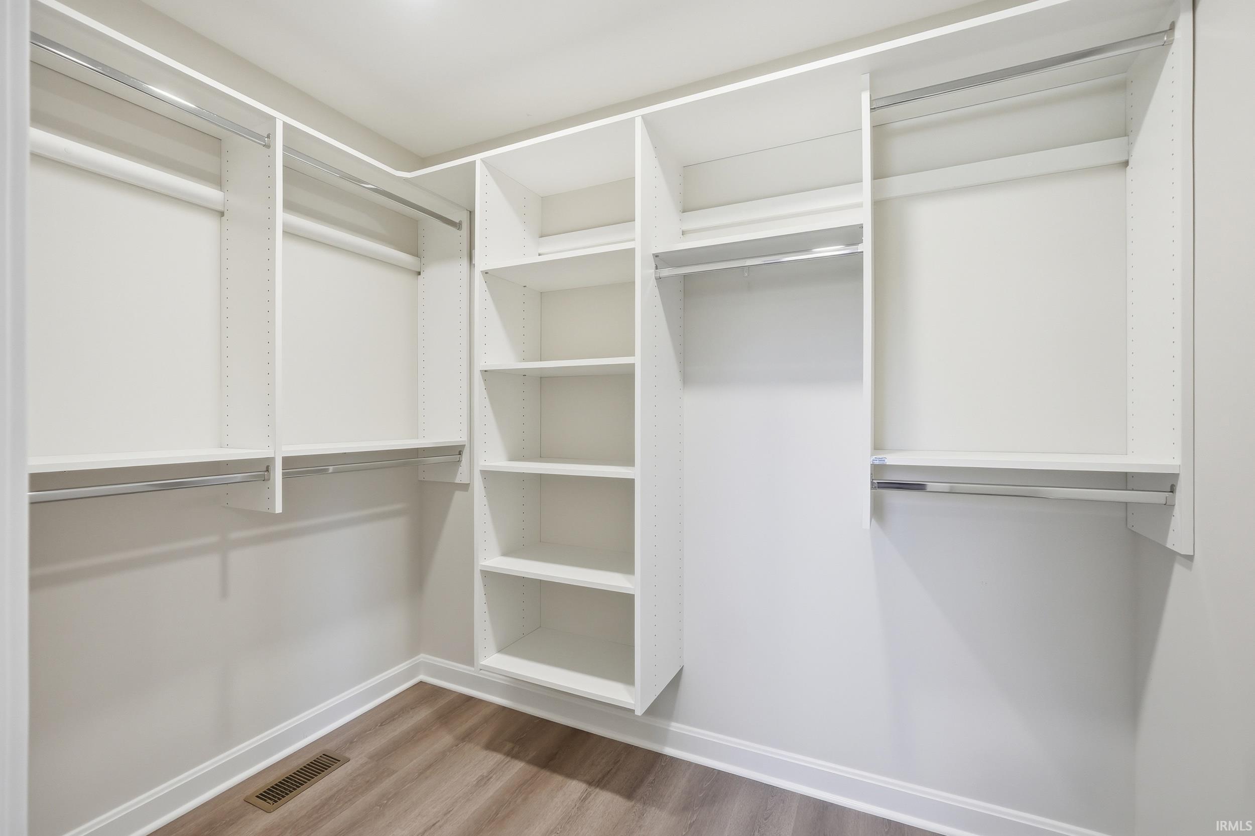Walk-in closet featuring white built-in shelving, multiple hanging rods, durable wood-finish flooring, and crisp white baseboards
