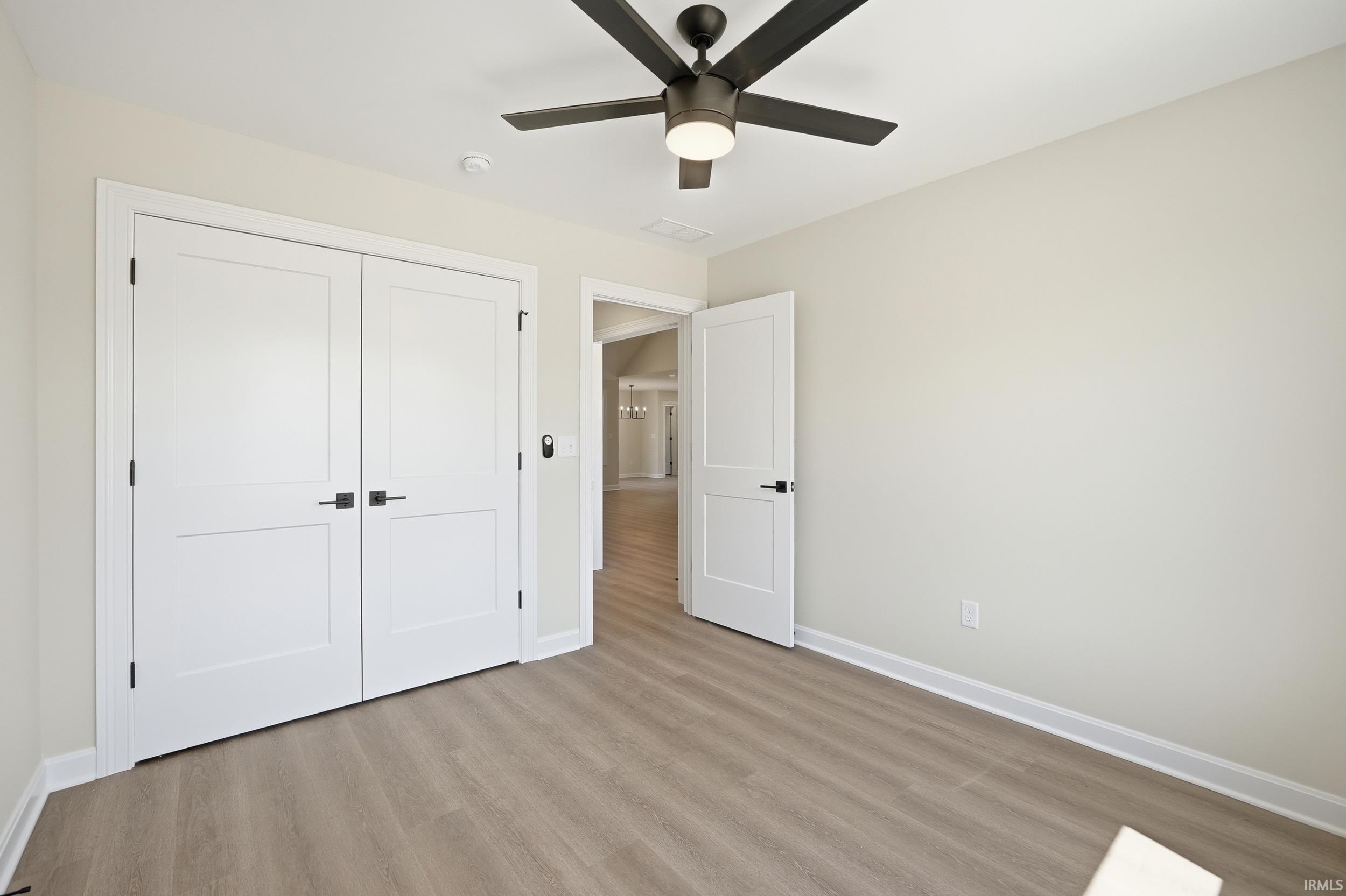 Room featuring wood-finish flooring, a ceiling fan with integrated lighting, and white baseboard trim
