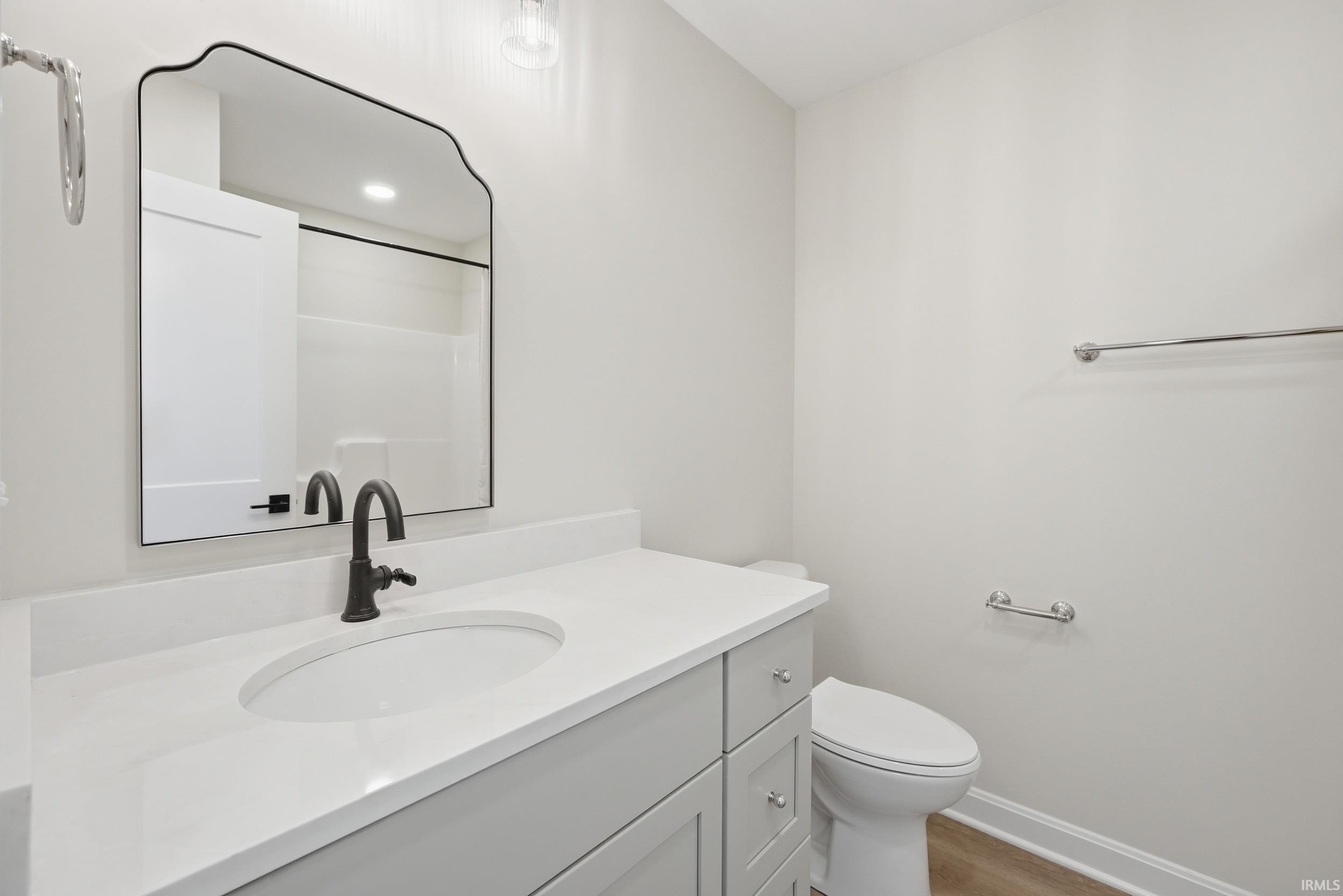 Bathroom featuring a light gray vanity with an integrated white sink, a solid surface countertop, matte black faucet, and a decorative framed mirror