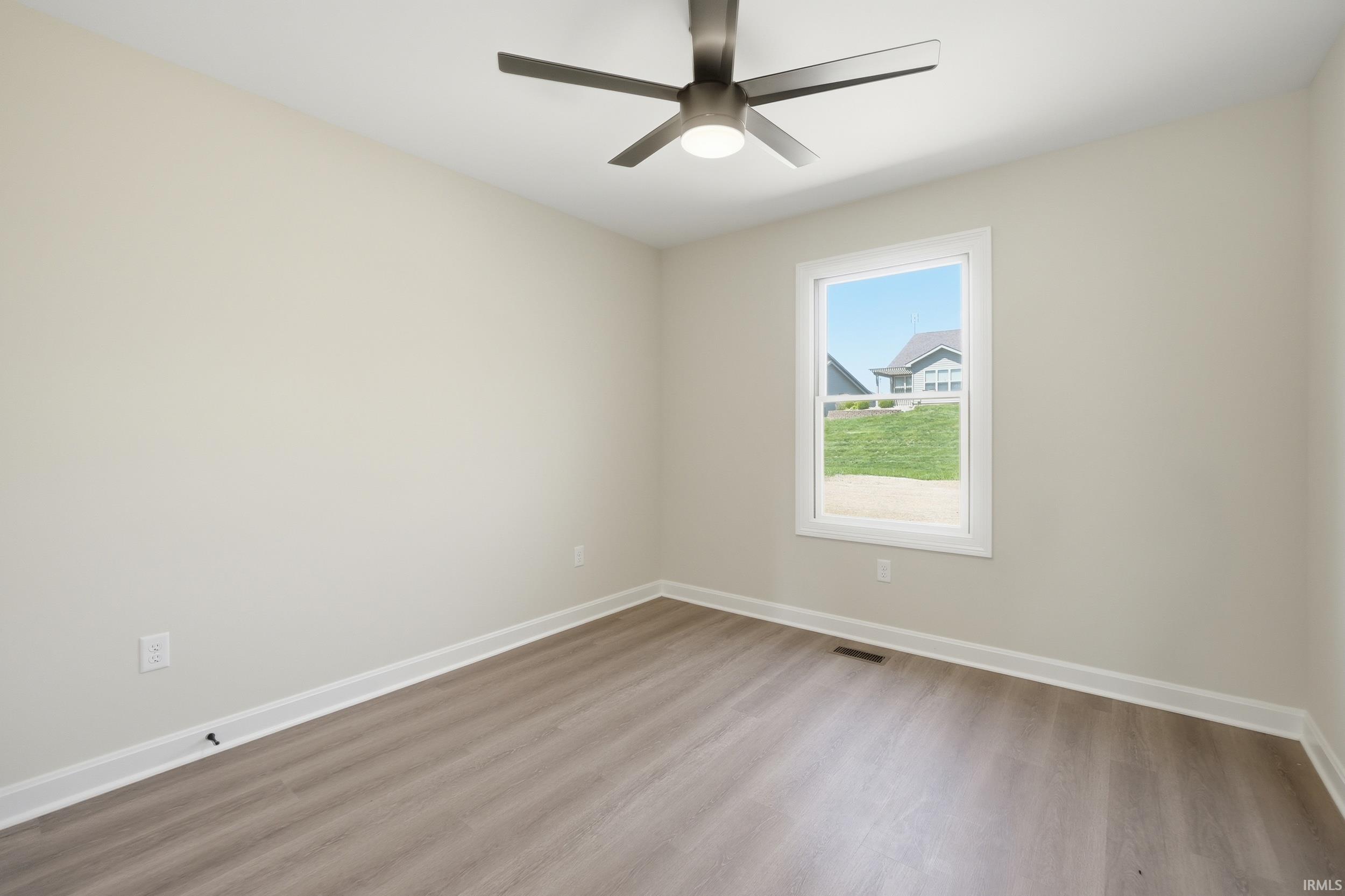 Spacious room featuring wood-finish flooring, white baseboards, and neutral wall paint