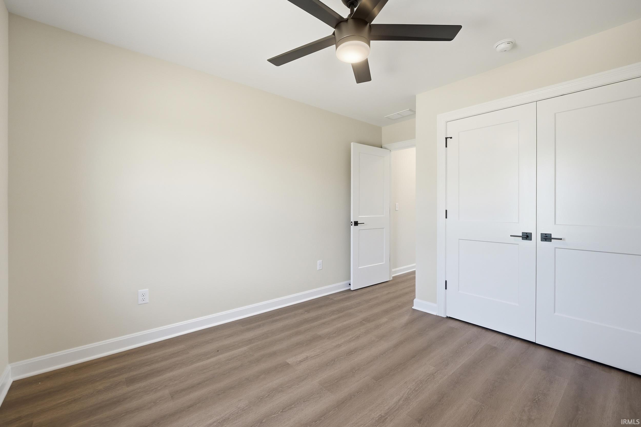 Room featuring wood-finish flooring, a ceiling fan with integrated lighting, and a double-door closet with matte black hardware