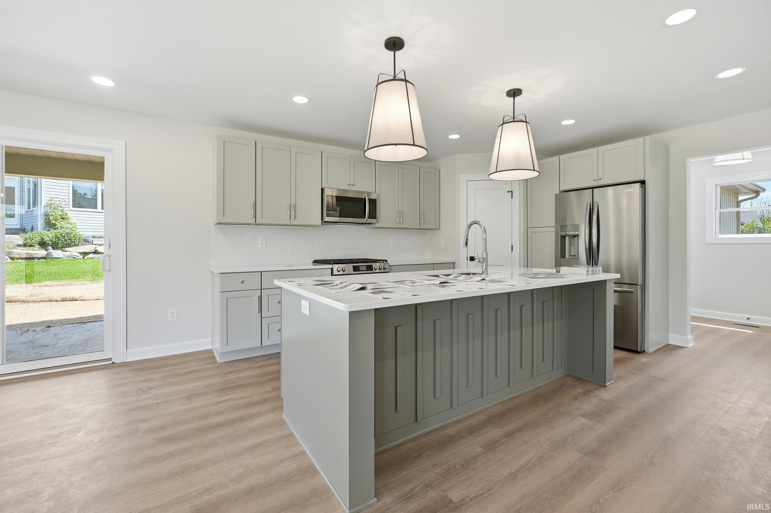 Kitchen featuring a central island with paneling, pendant lighting, stainless steel appliances, light-toned cabinetry, and wood-finish flooring