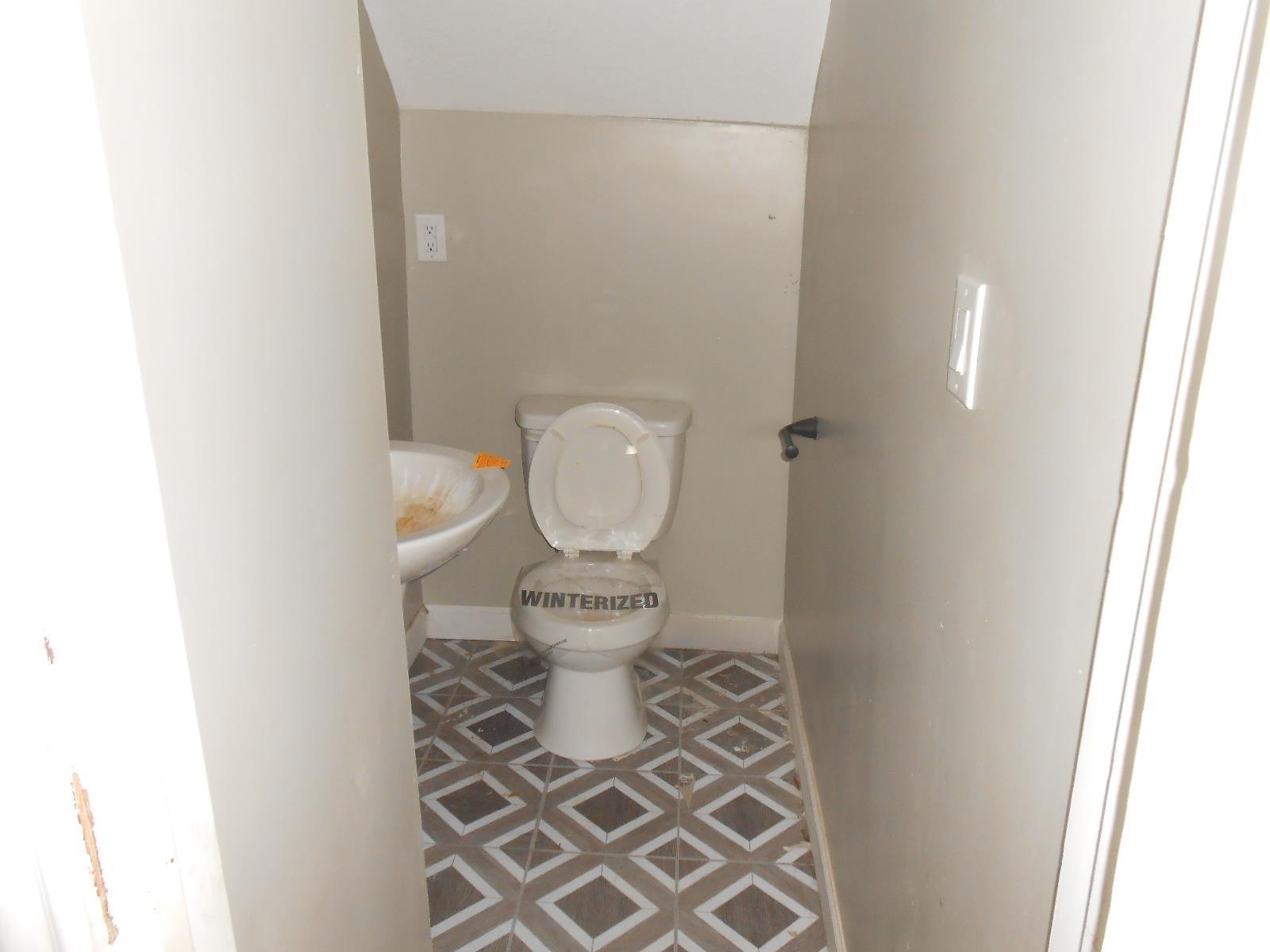 Compact bathroom featuring geometric tile flooring, a pedestal sink, and a toilet