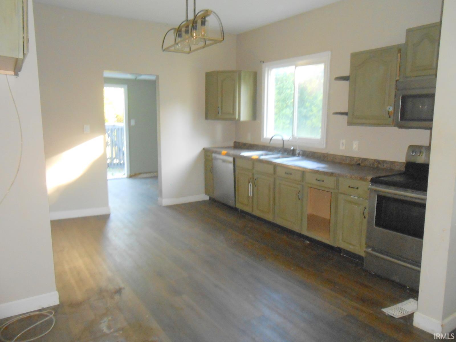 Kitchen area featuring wood-finish flooring, a window, green cabinetry with a countertop, a stainless steel range, and a stainless steel microwave