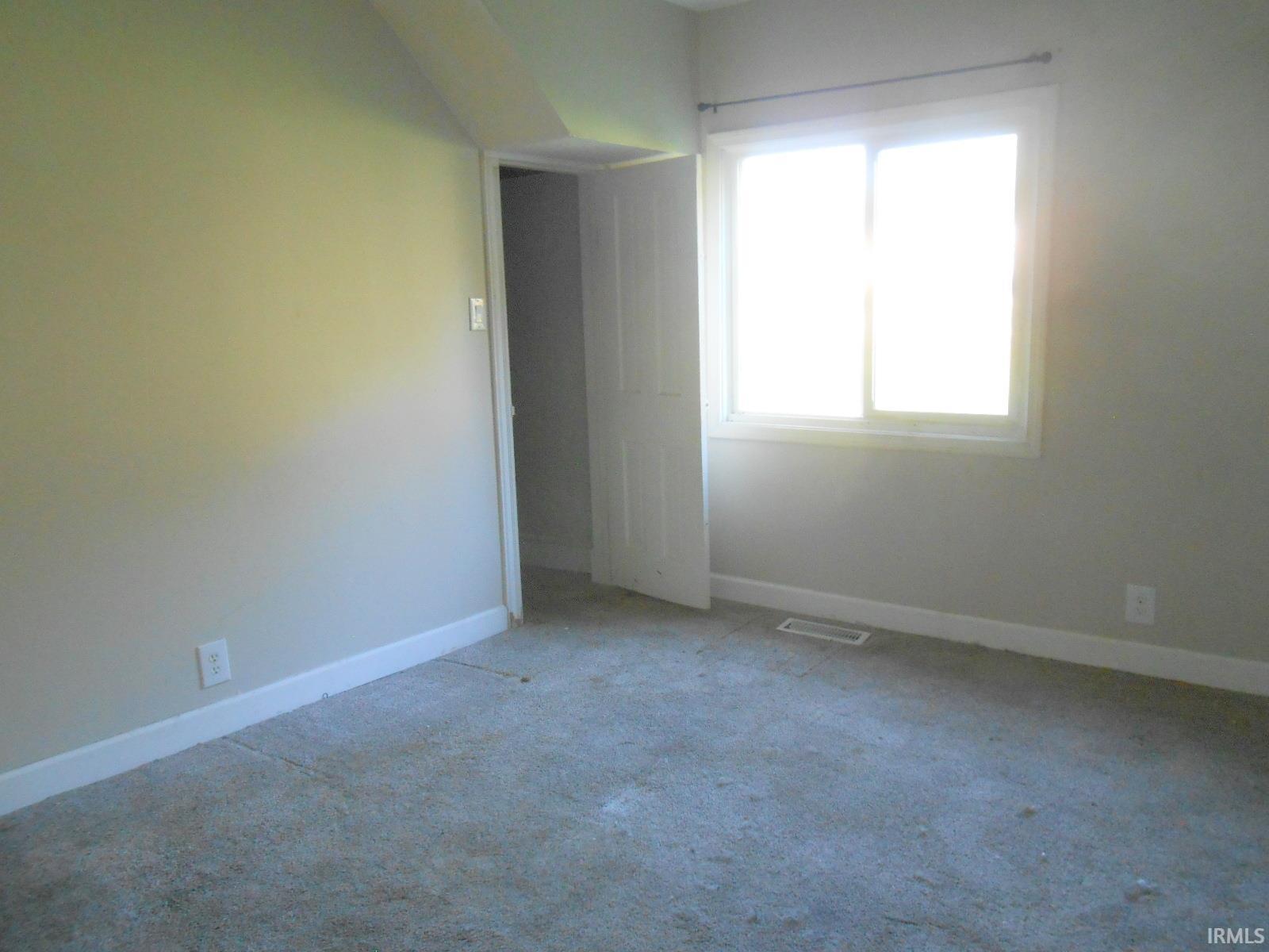 Carpeted interior space featuring a window with white trim, baseboard molding, a white interior door, and a wall outlet