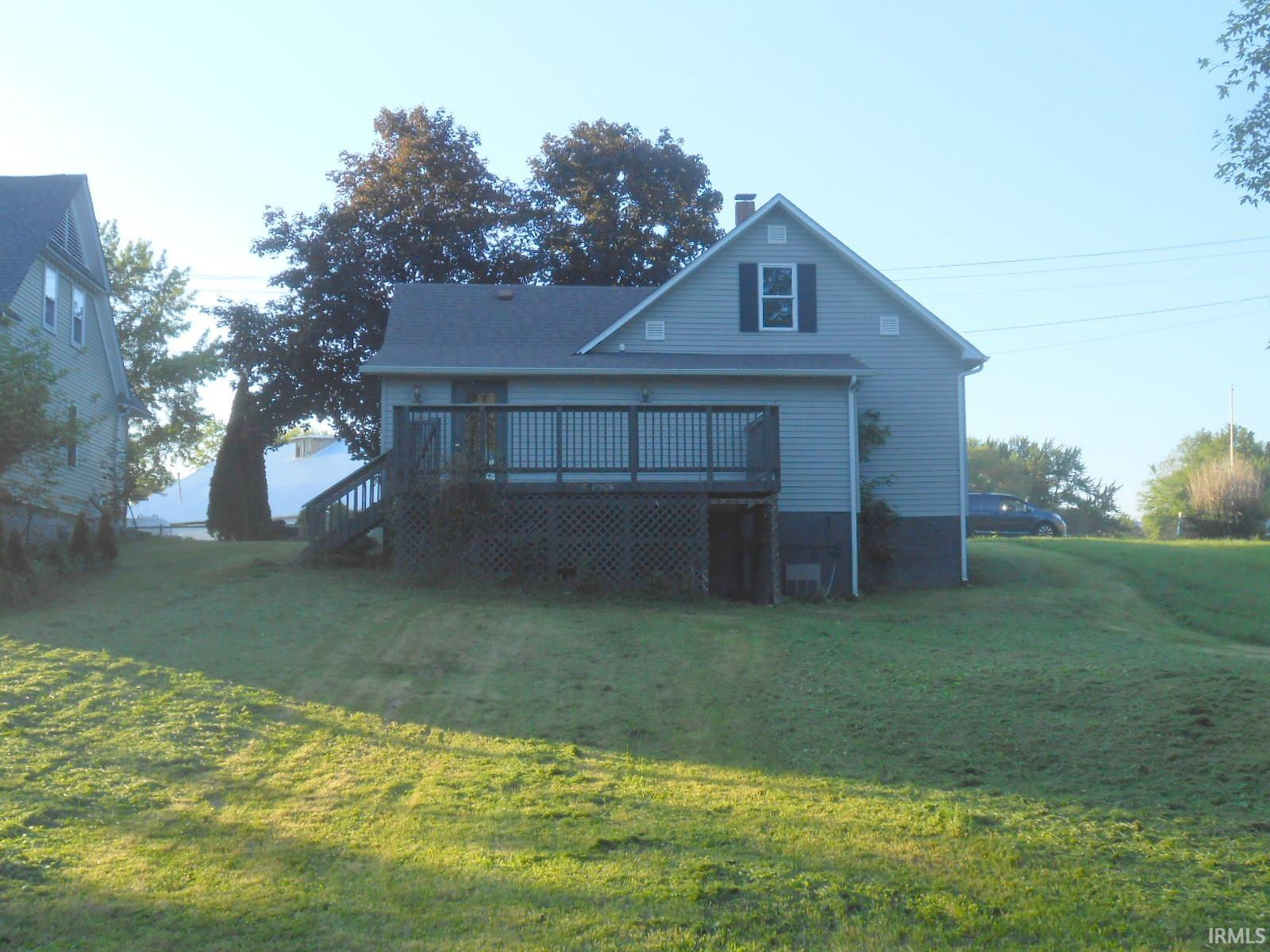 Rear exterior featuring a spacious wooden deck with lattice skirting, light blue vinyl siding, and a gabled roofline