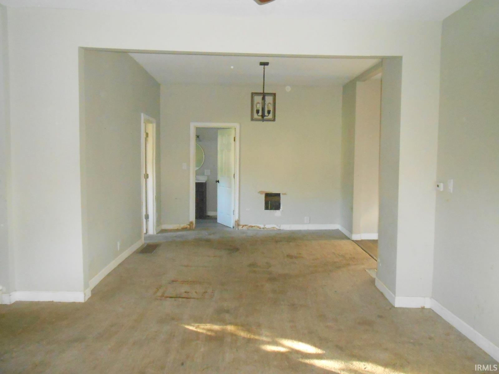 Spacious interior room with a modern hanging light fixture and a visible doorway to a bathroom featuring a circular mirror and vanity