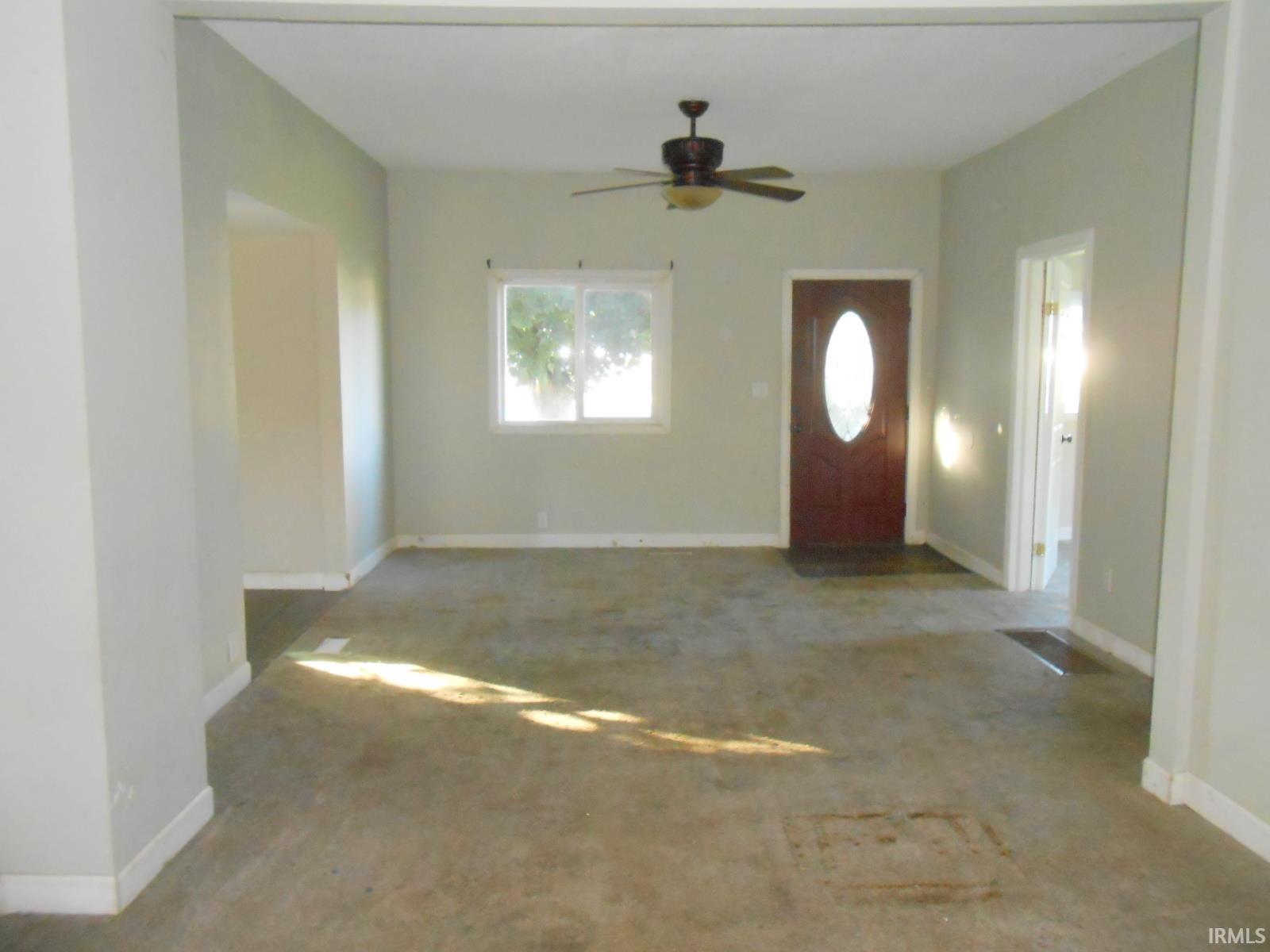 Open concept living area with a brown oval-lite entry door, single window, and ceiling fan
