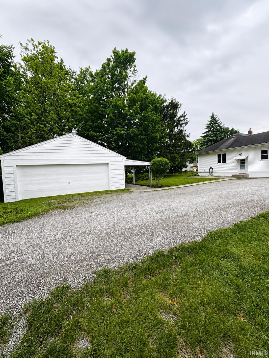 Detached garage with white horizontal siding and a gravel driveway