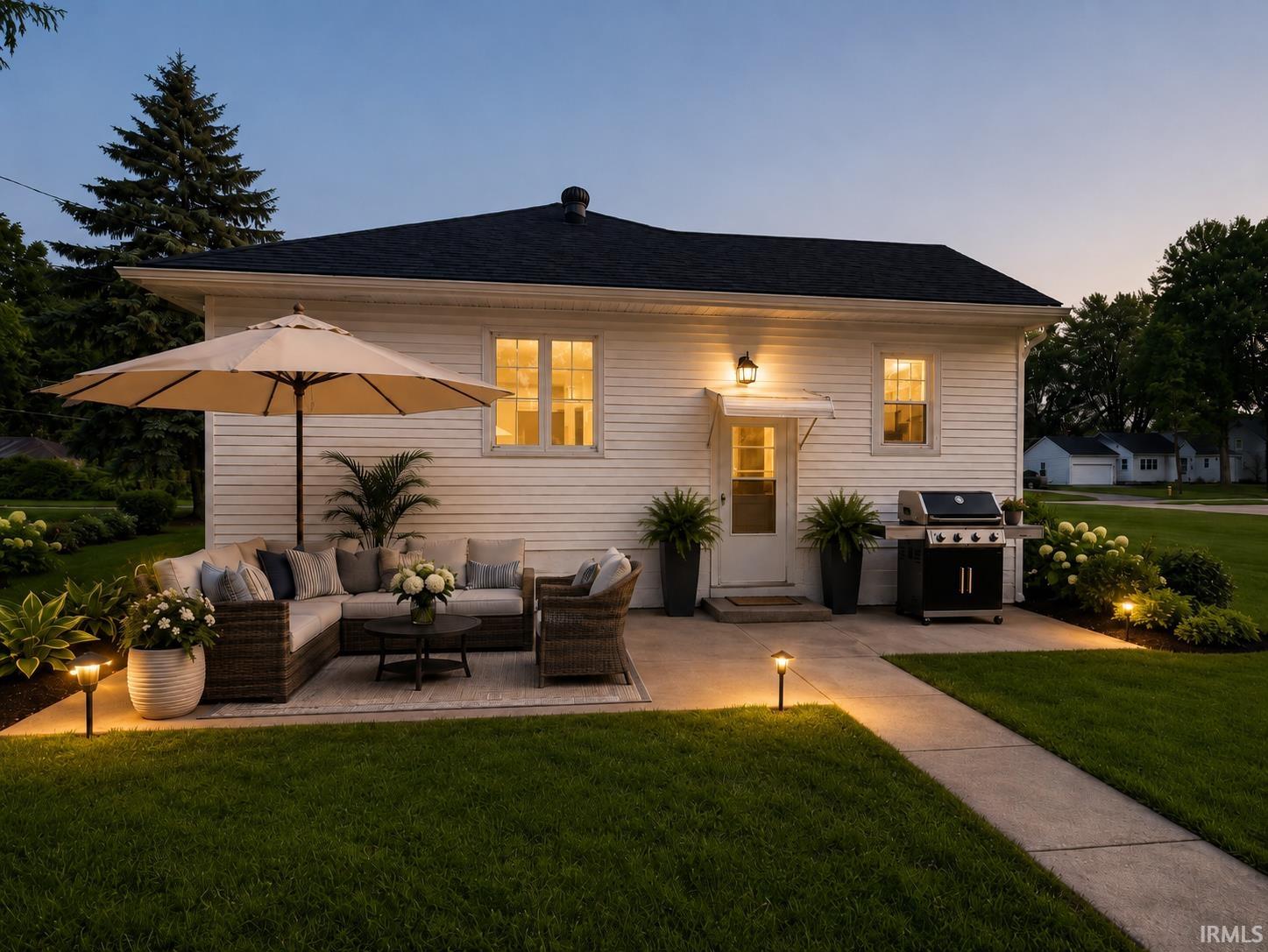 Rear exterior featuring a concrete patio, landscaped garden beds, and ground-level lighting Displaying original and virtually staged interior images of the property