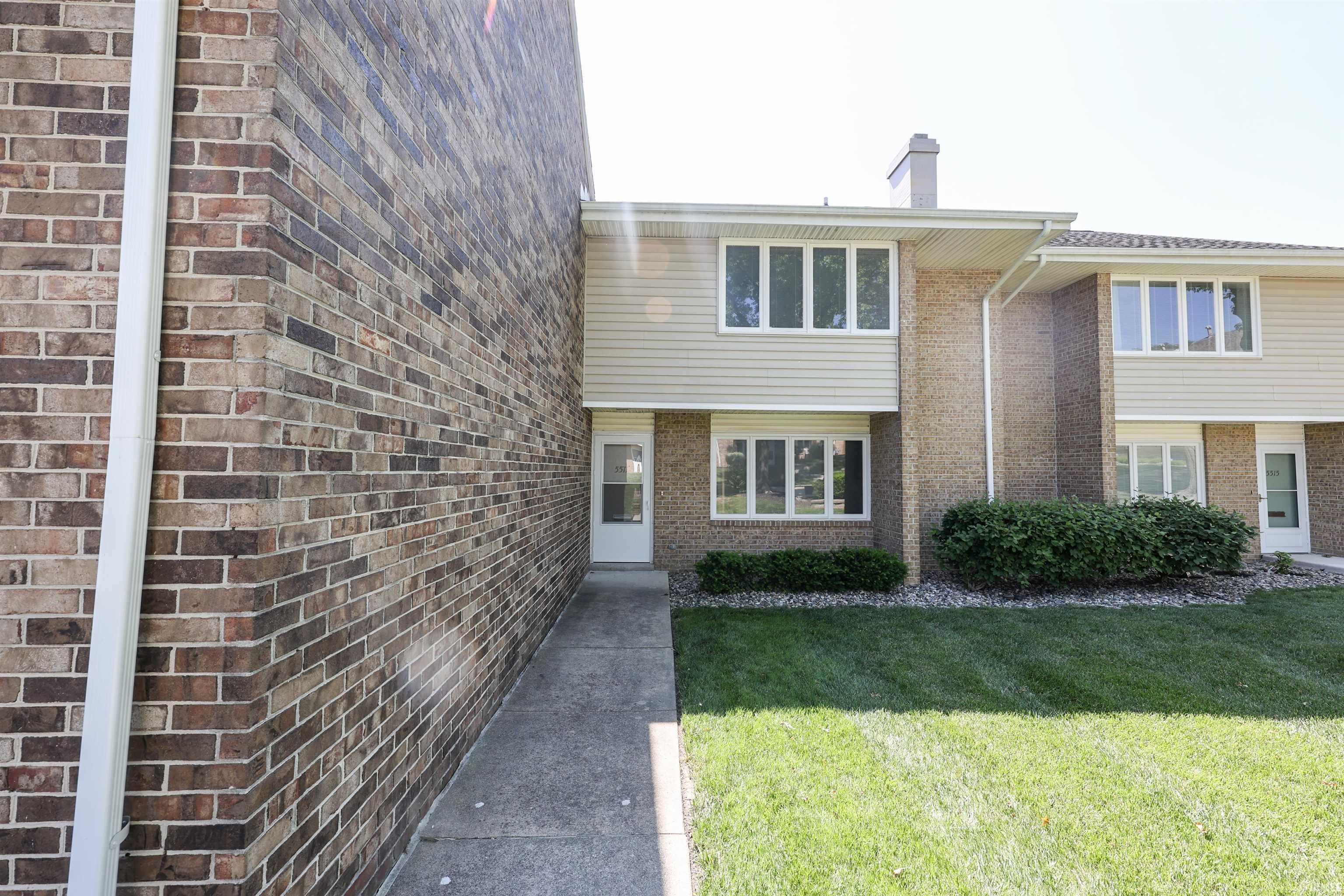 Brick and siding exterior featuring white frame windows, a white entry door, and a concrete walkway