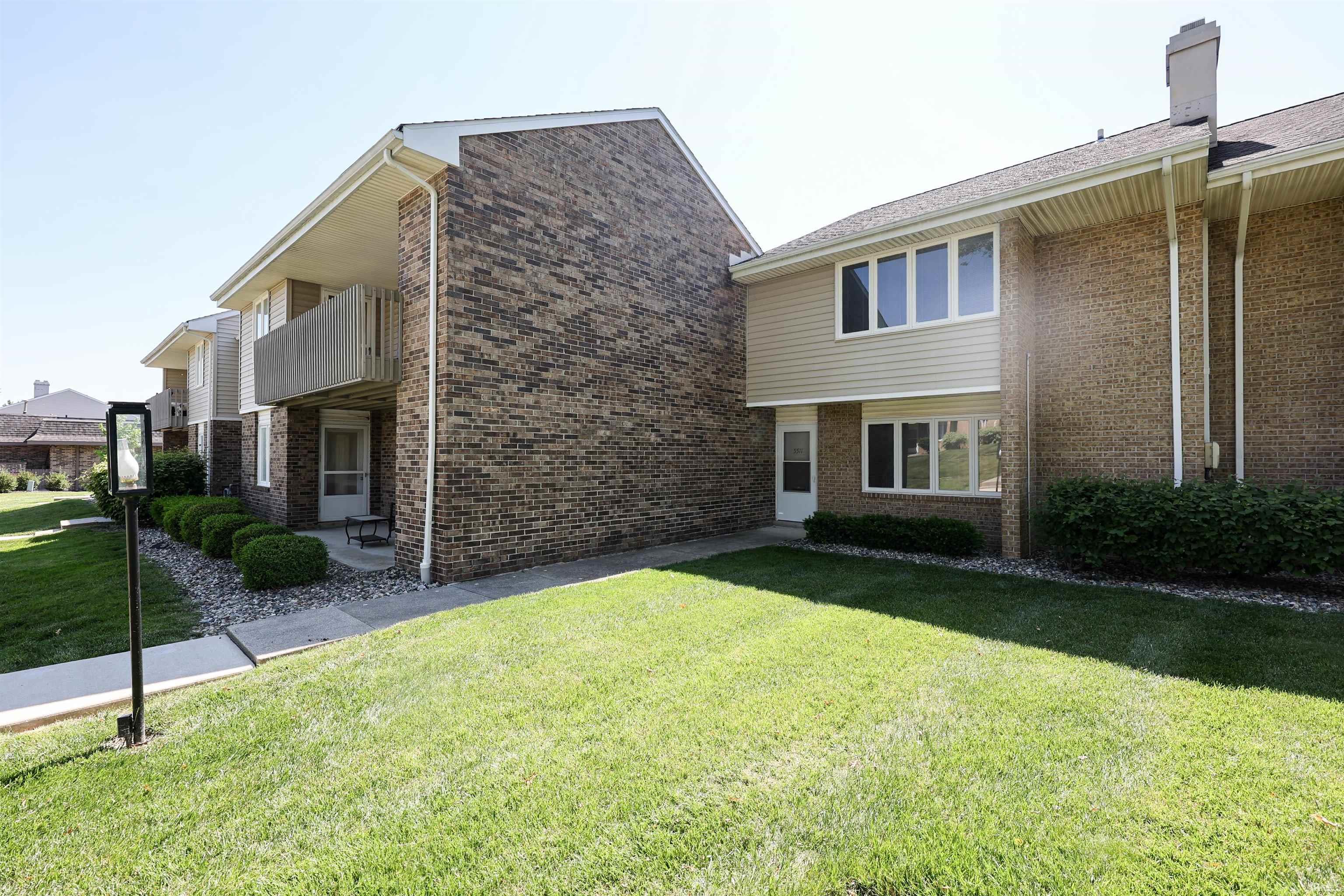 Exterior facade with brick and horizontal siding, featuring multiple windows, a private balcony, and a manicured lawn