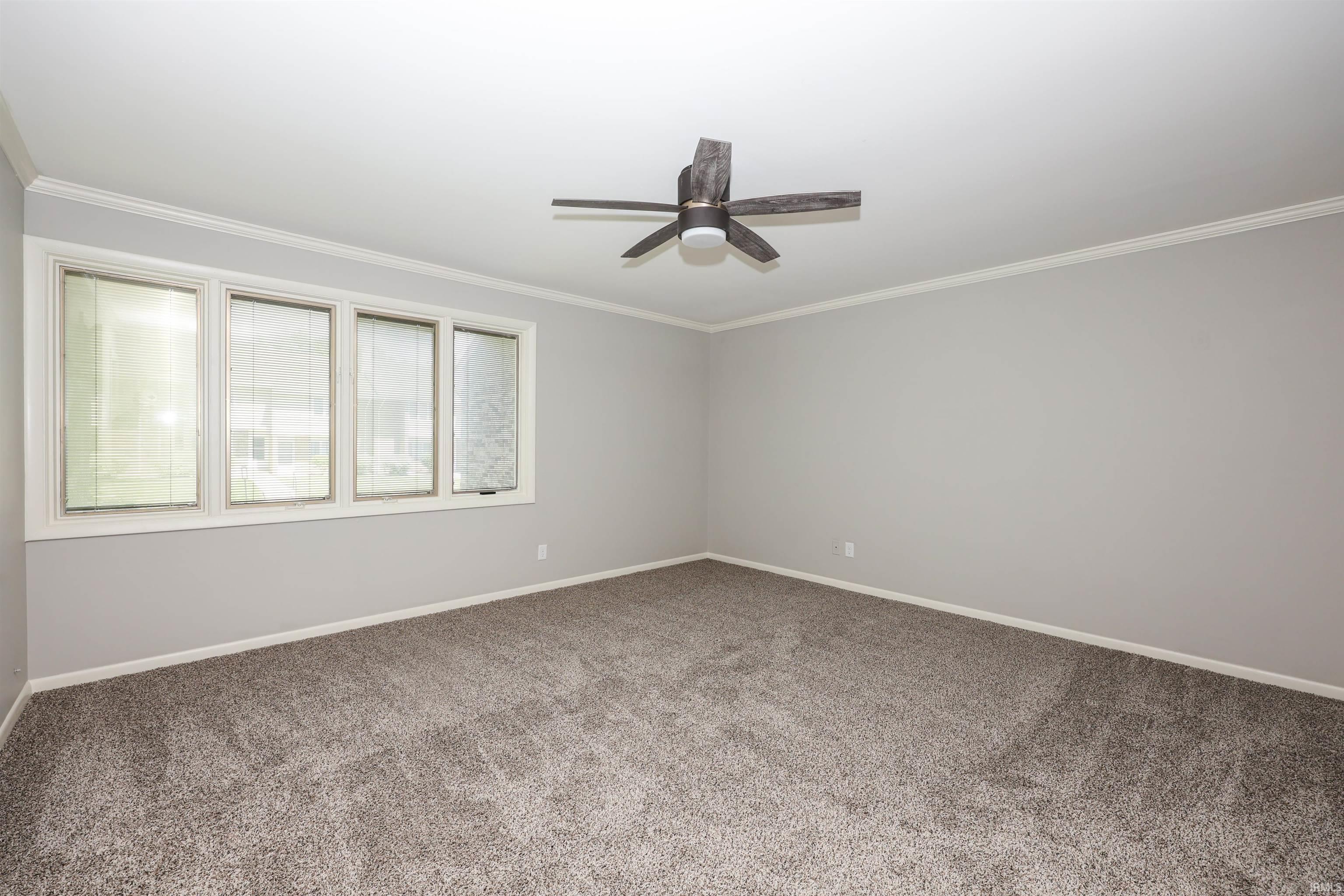 Spacious room featuring gray carpet, light gray walls, white trim, and a ceiling fan with integrated lighting