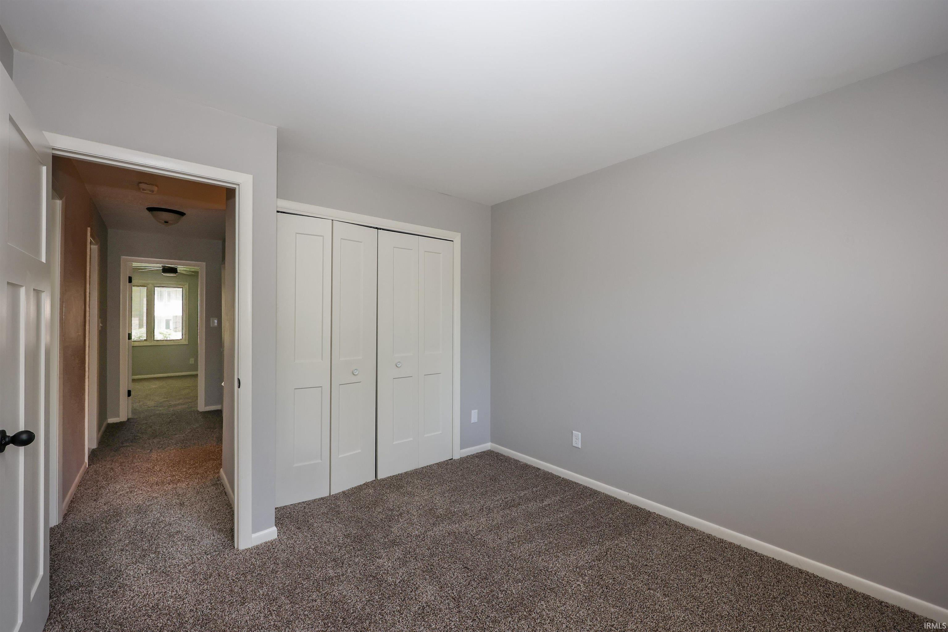 Carpeted room featuring light gray walls, white trim, and a bi-fold closet with panel doors