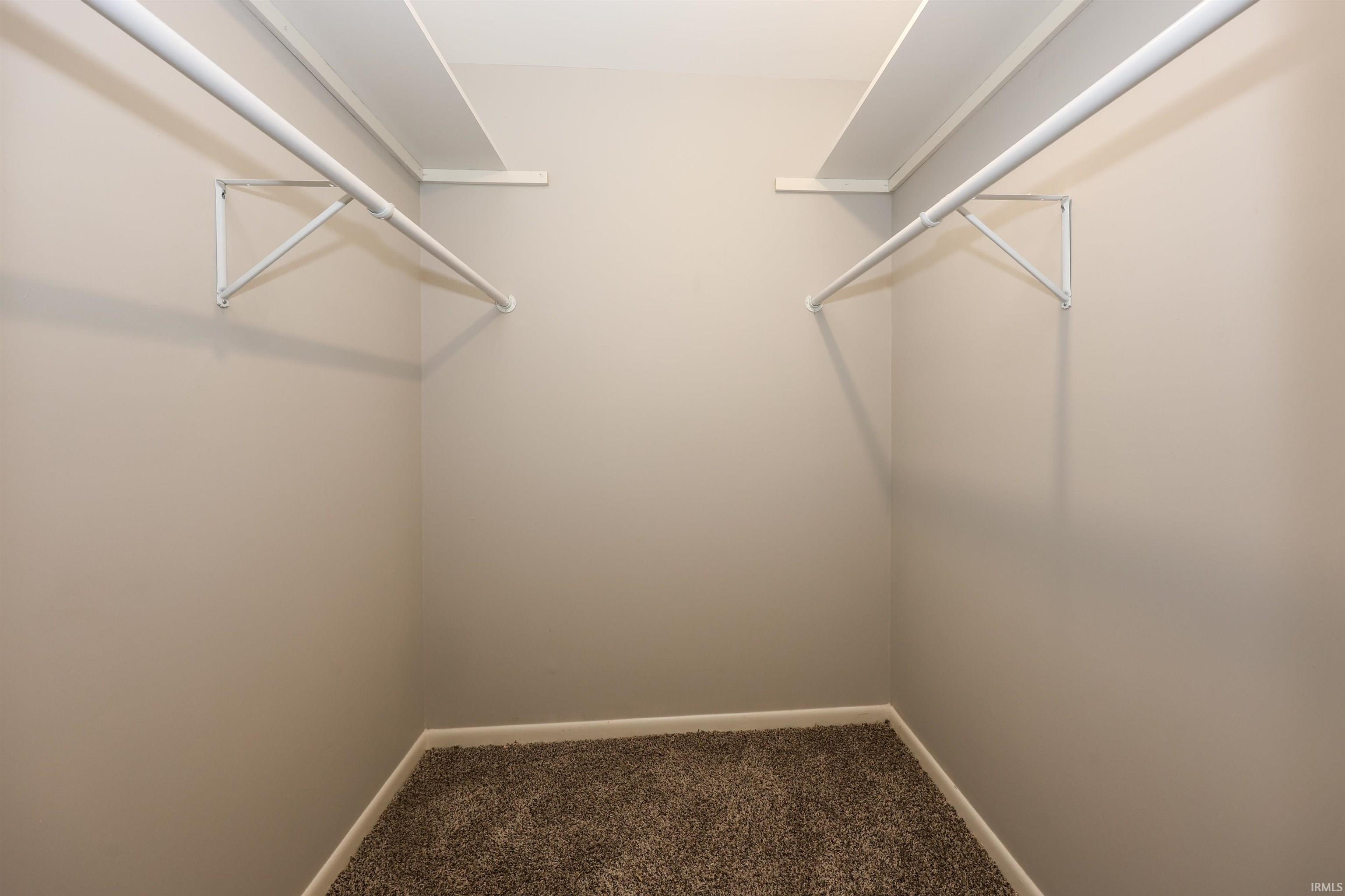 Interior closet featuring a neutral wall color, white shelving, white hanging rods, and textured carpeting