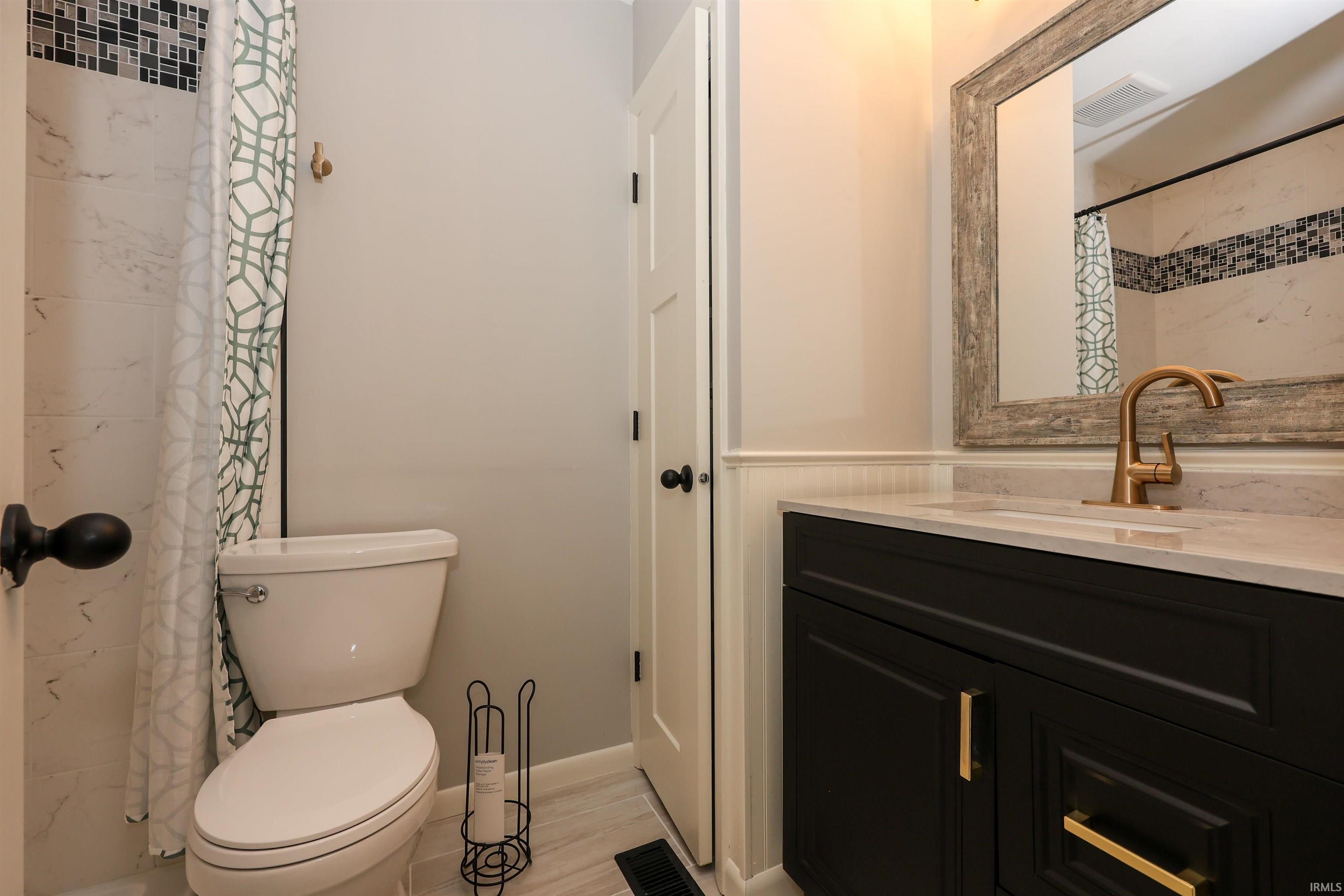 Bathroom featuring a dark wood vanity with gold-tone hardware, a white countertop, and a distressed wood-frame mirror