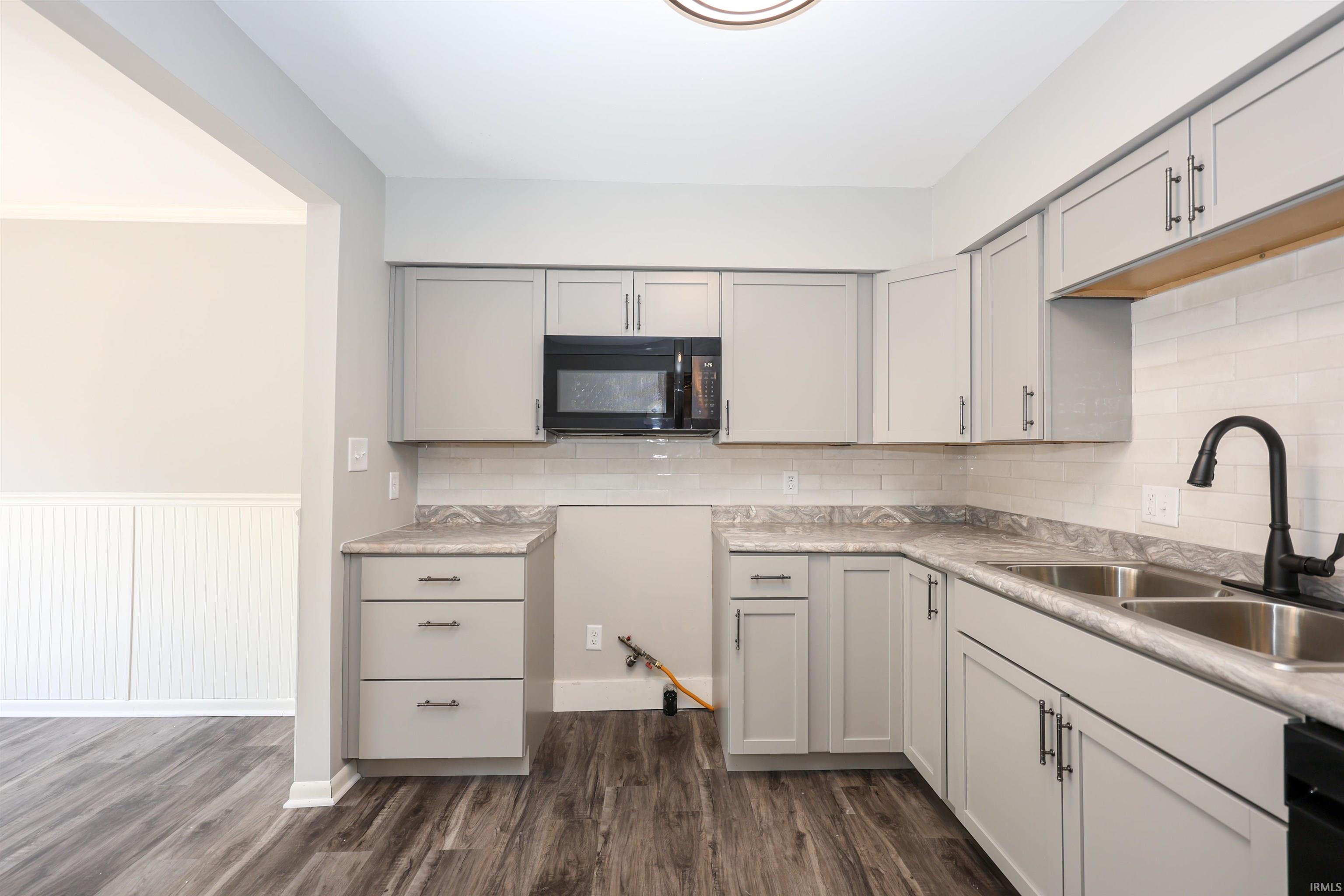 Modern kitchen featuring light gray cabinetry, stainless steel double basin sink with a matte black faucet, and patterned countertops