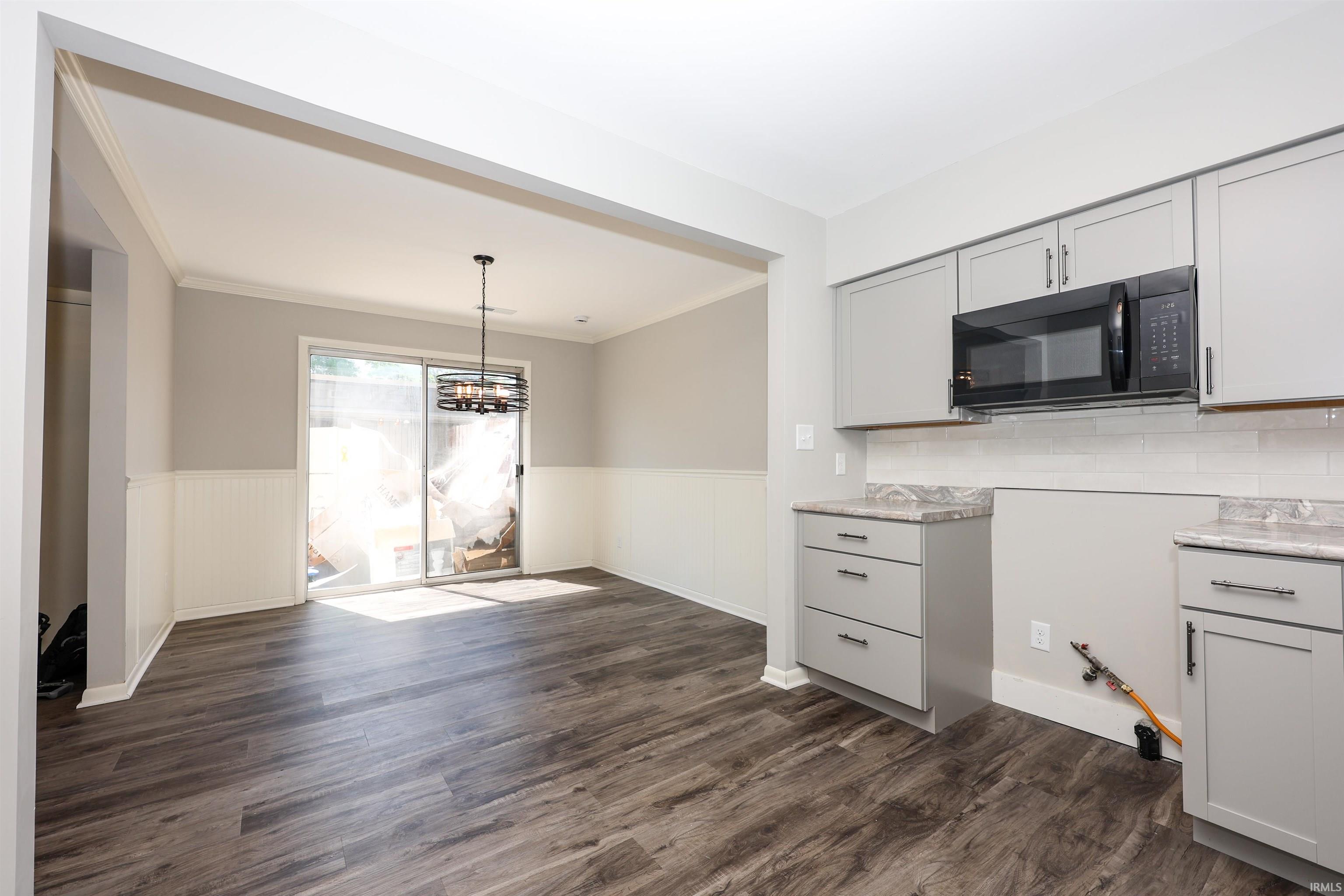 Open-concept kitchen and dining area featuring wood-finish flooring, light gray cabinetry, and white subway tile backsplash