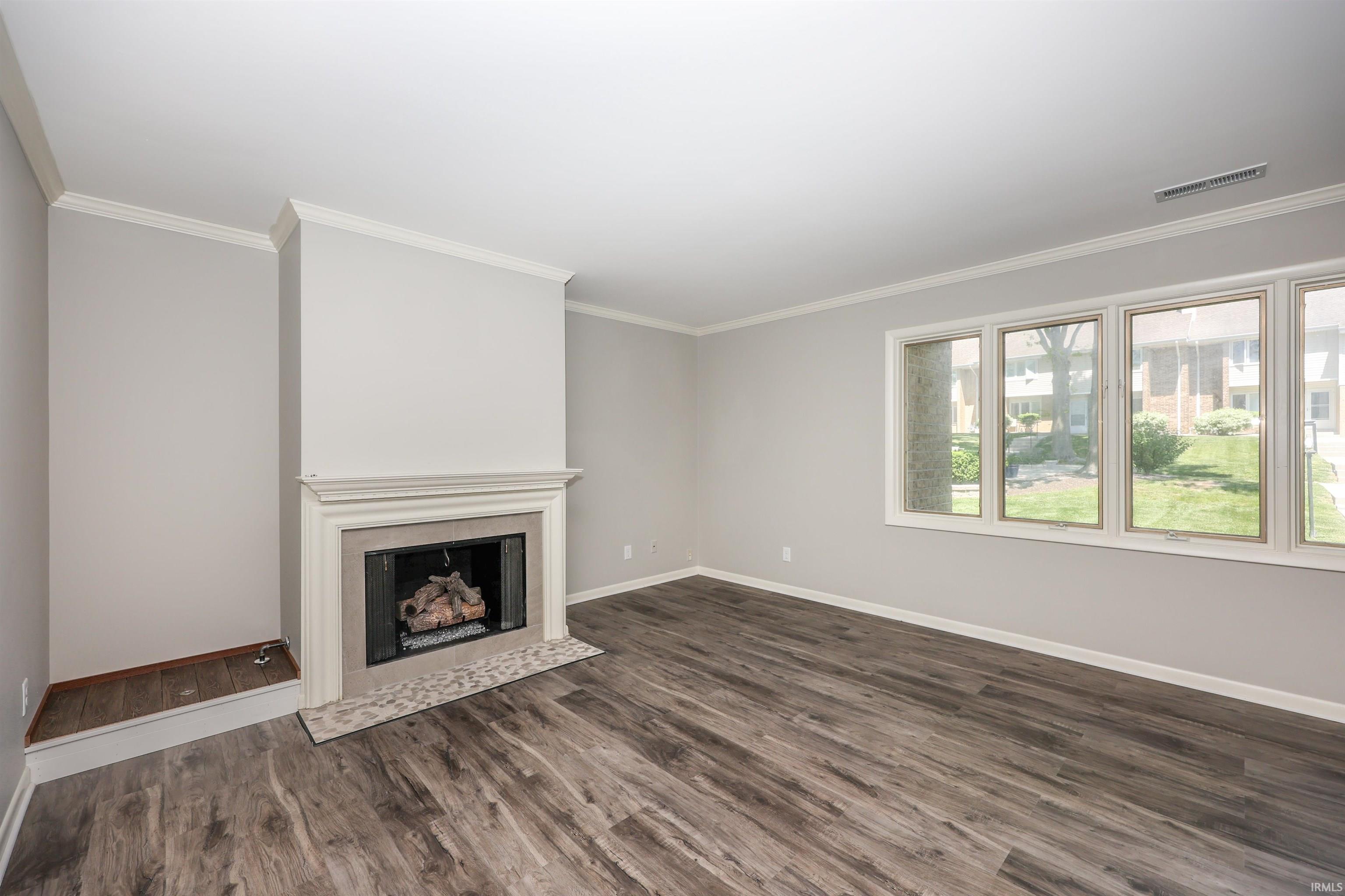 Spacious living area featuring a fireplace with a decorative mantel and hearth, wood-finish flooring, and multiple windows providing ample natural light