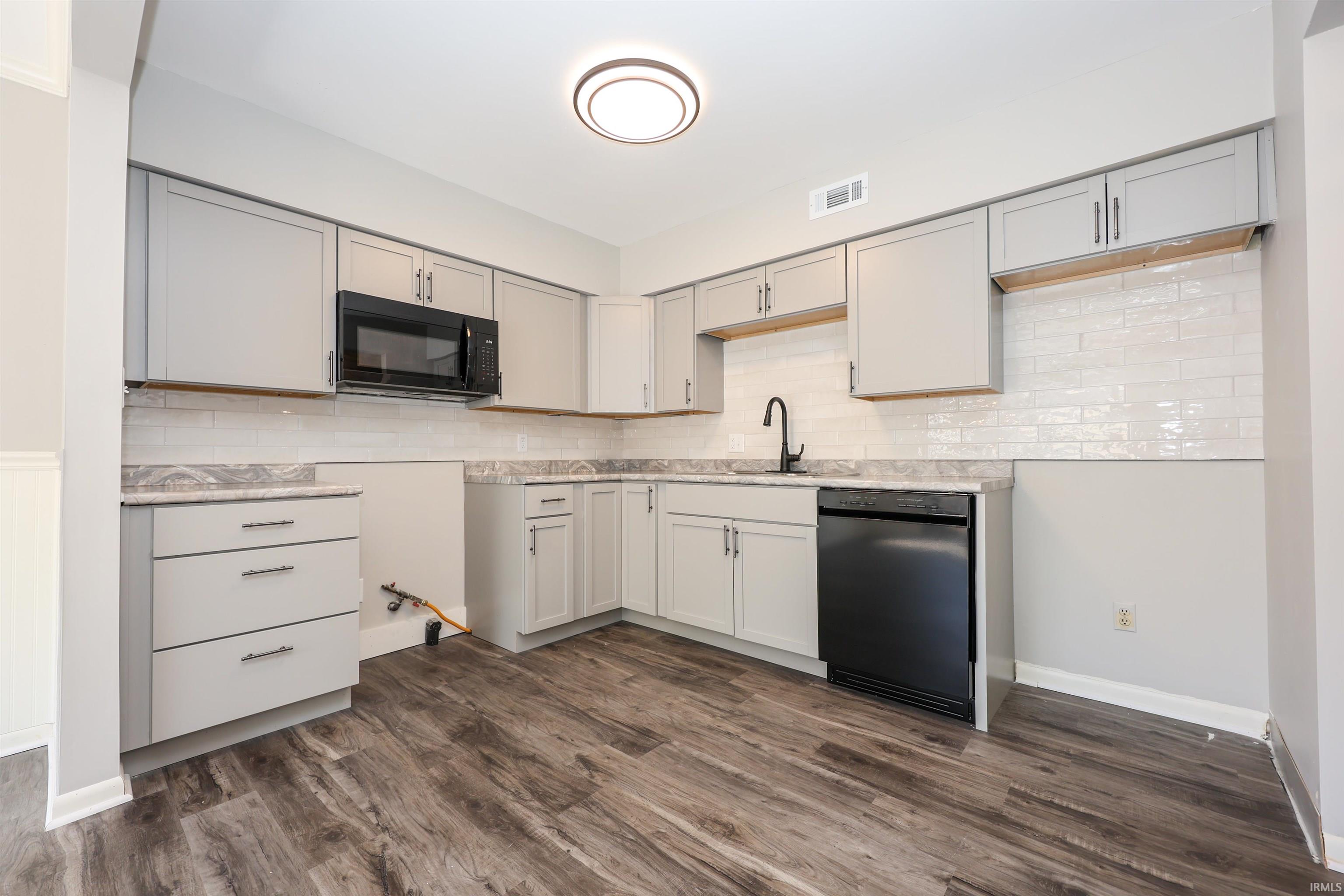 Kitchen featuring light gray cabinetry, dark wood-finish flooring, white subway tile backsplash, and dark countertops