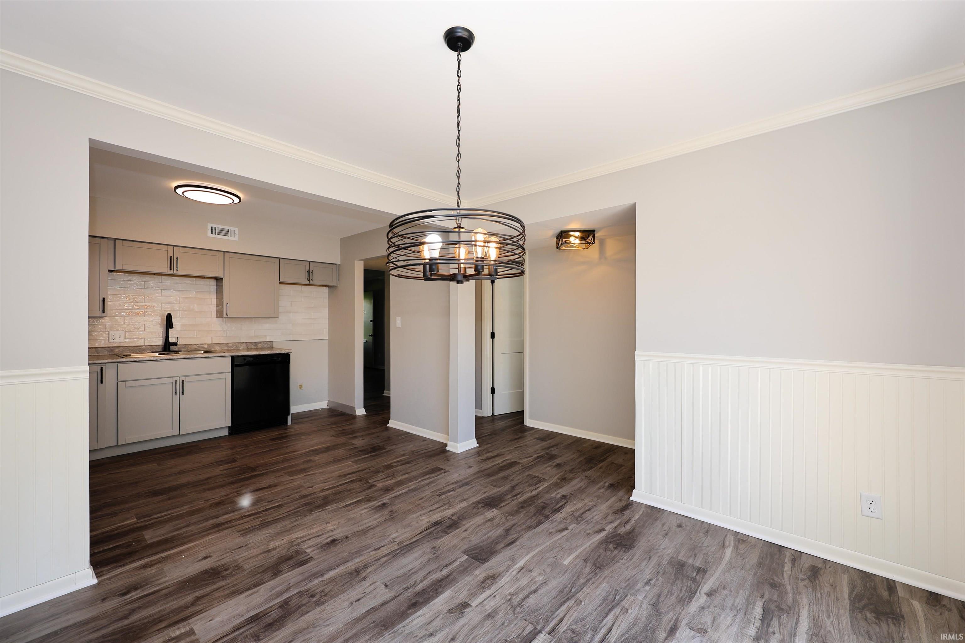 Spacious open-concept room featuring wood-finish flooring, a contemporary chandelier, and white wainscoting