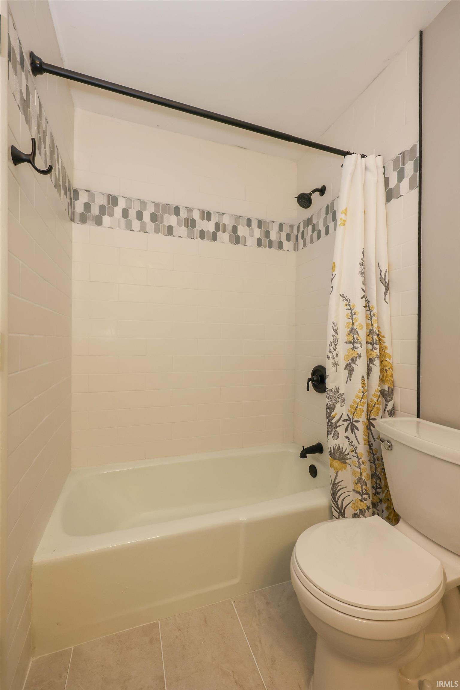 Bathtub and shower combination featuring white subway tile surround, decorative mosaic accent tile, and matte black fixtures