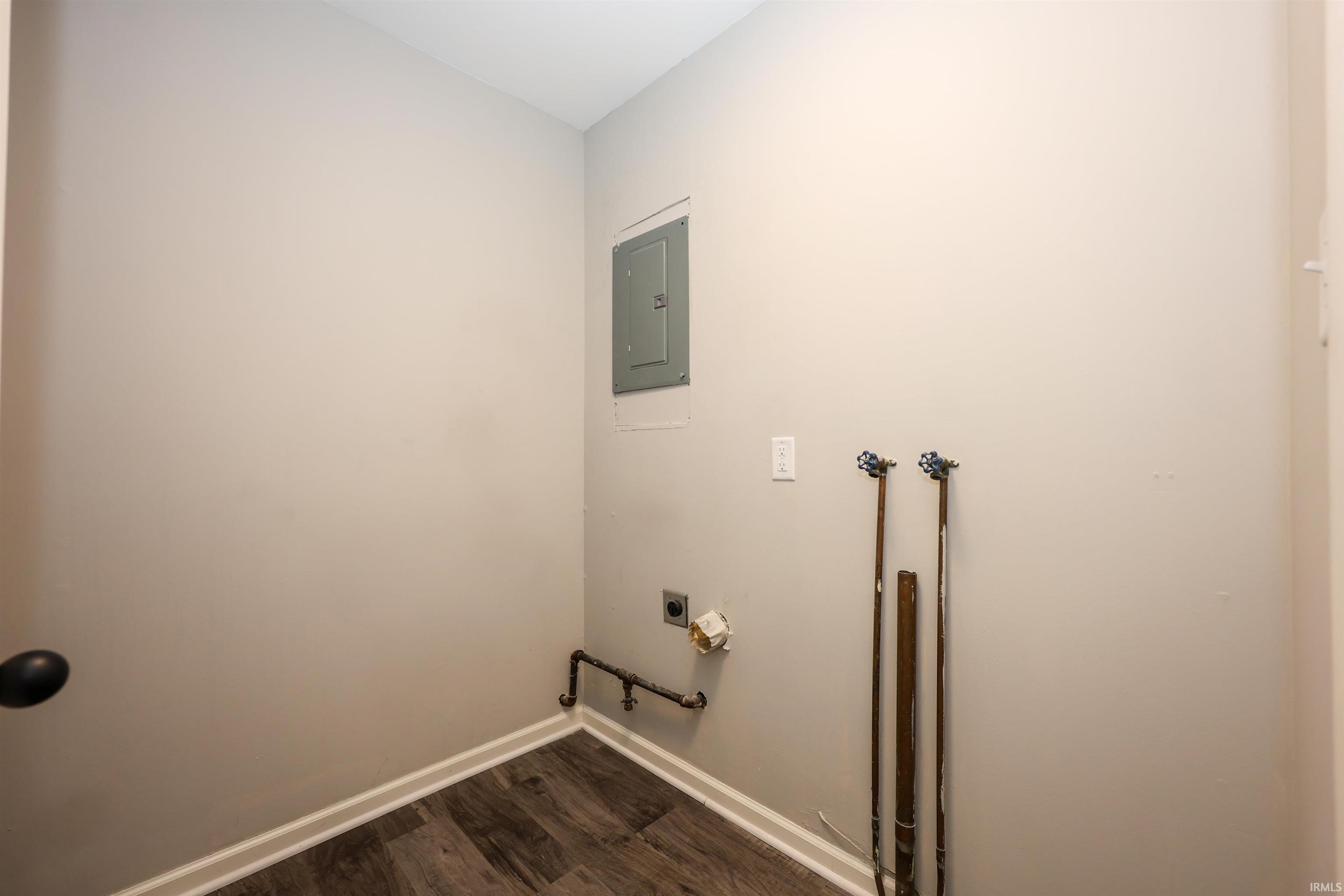 Utility area featuring wood-finish flooring, light gray walls, white baseboards, and a visible electrical panel