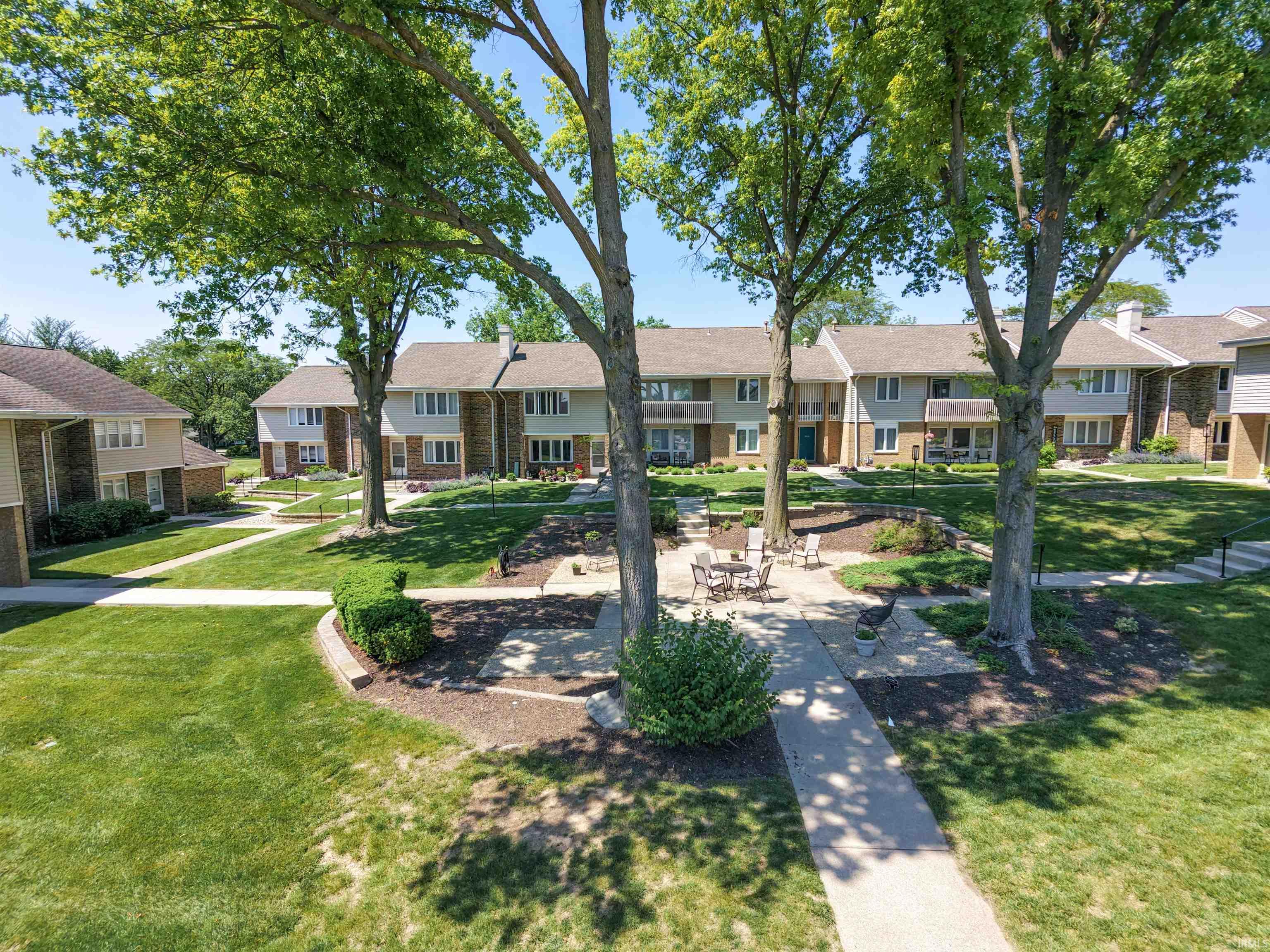 Manicured communal green space featuring mature trees and a stone patio with seating