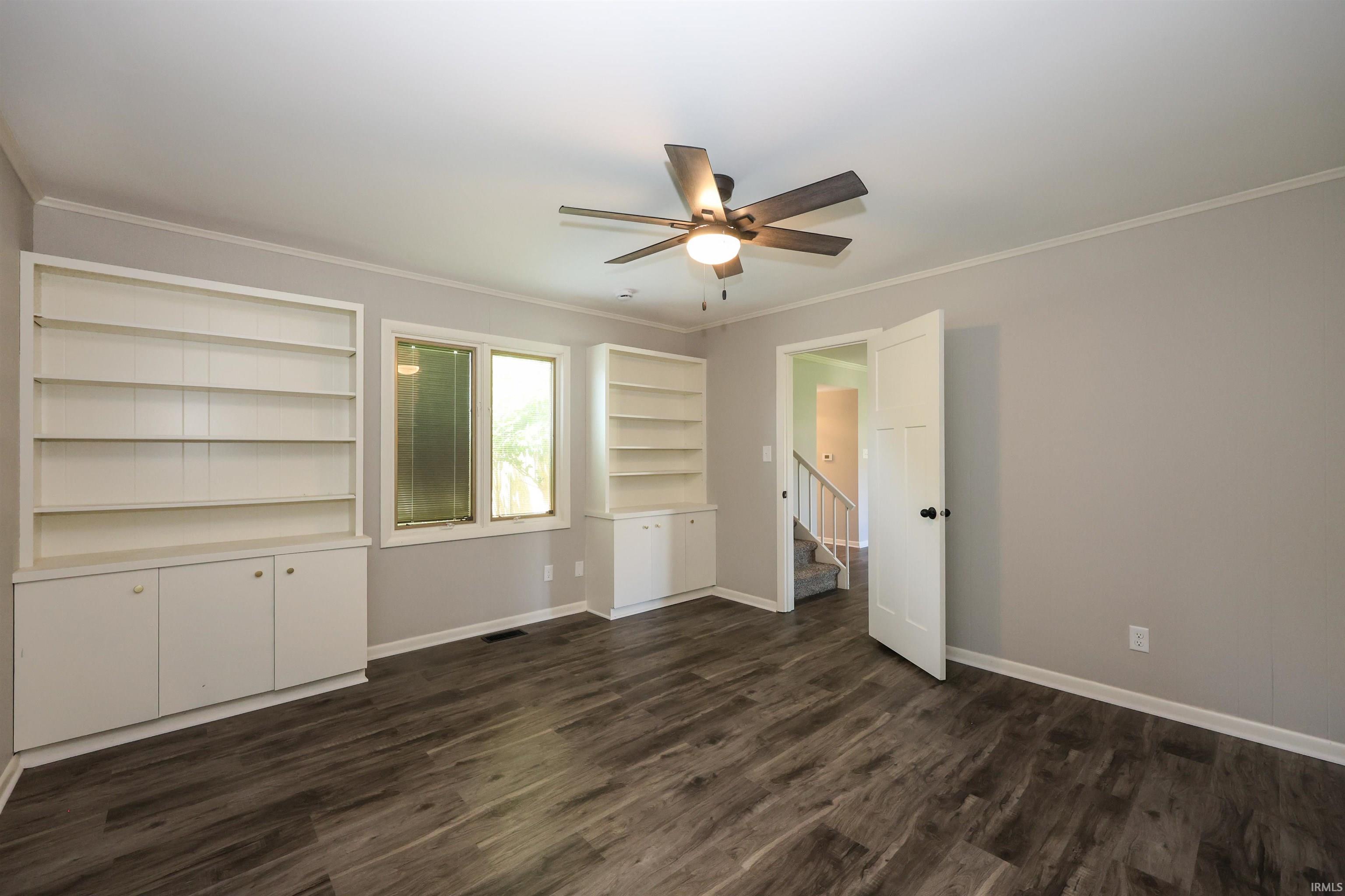 Room featuring wood-finish flooring, built-in shelving with lower cabinetry, and a ceiling fan with integrated lighting