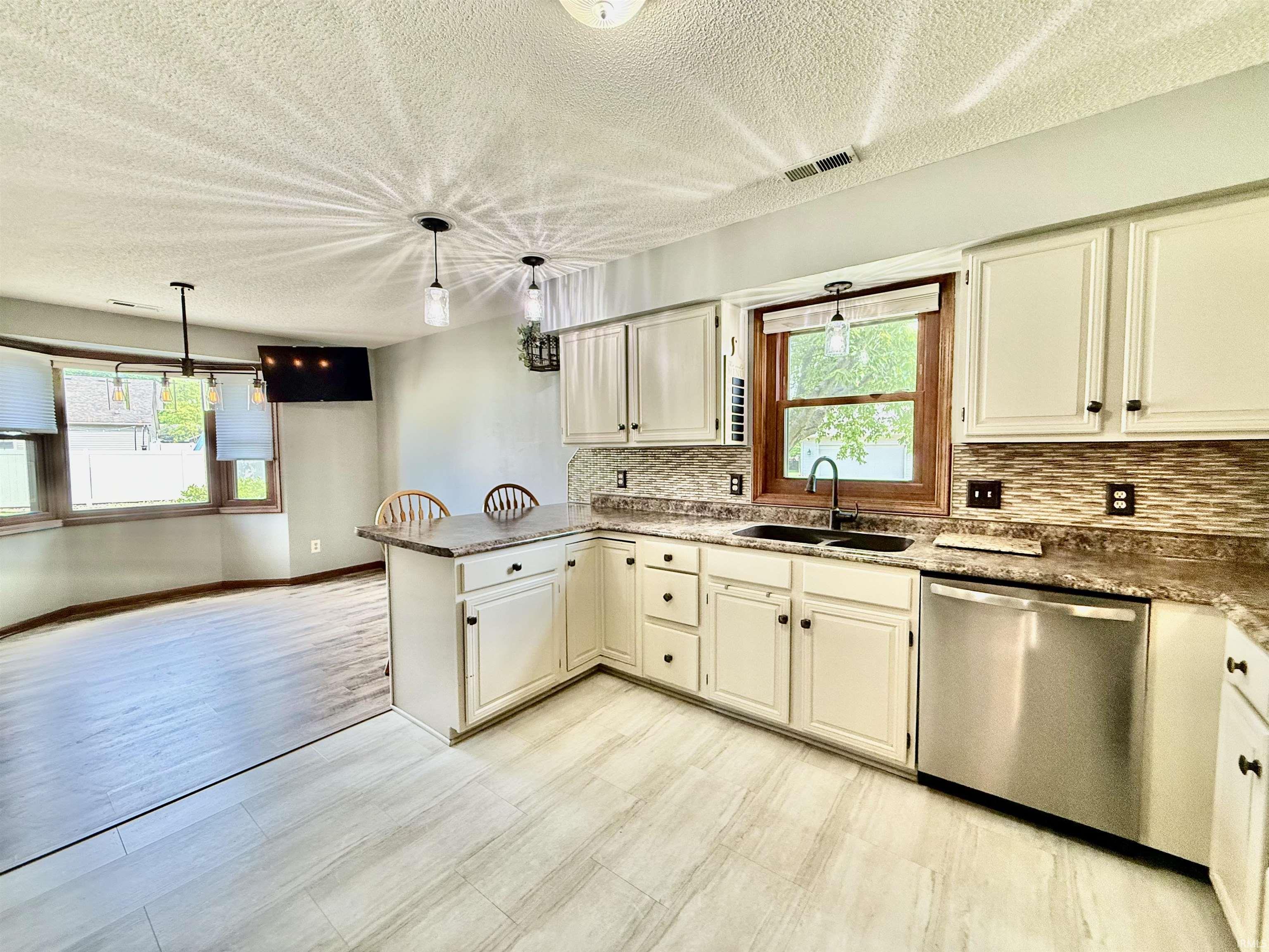 Kitchen featuring light cabinetry, a textured backsplash, dark countertops, and stainless steel appliances