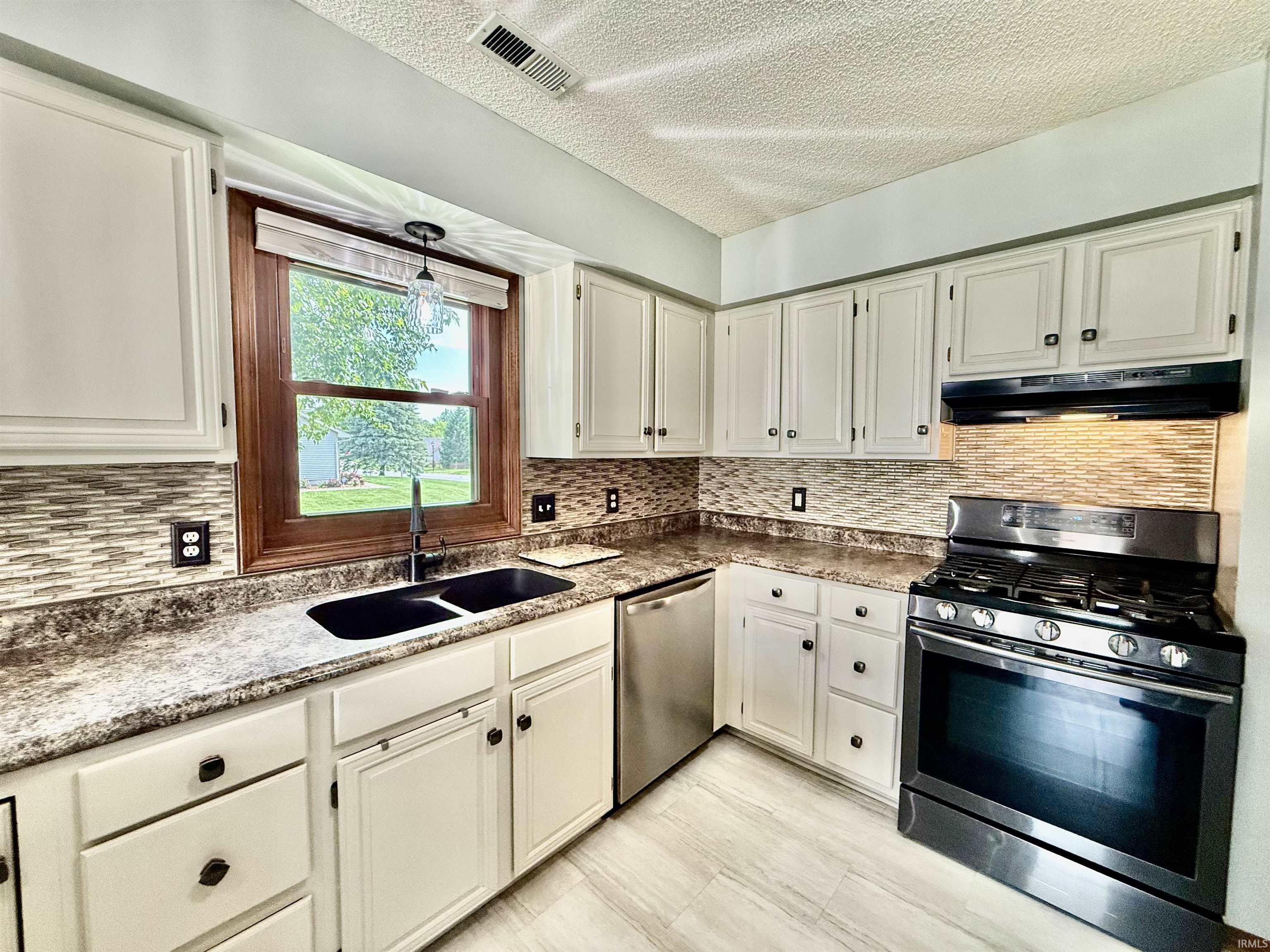 Kitchen featuring white cabinetry, mosaic tile backsplash, wood-finish countertops, stainless steel appliances, and light wood-finish flooring