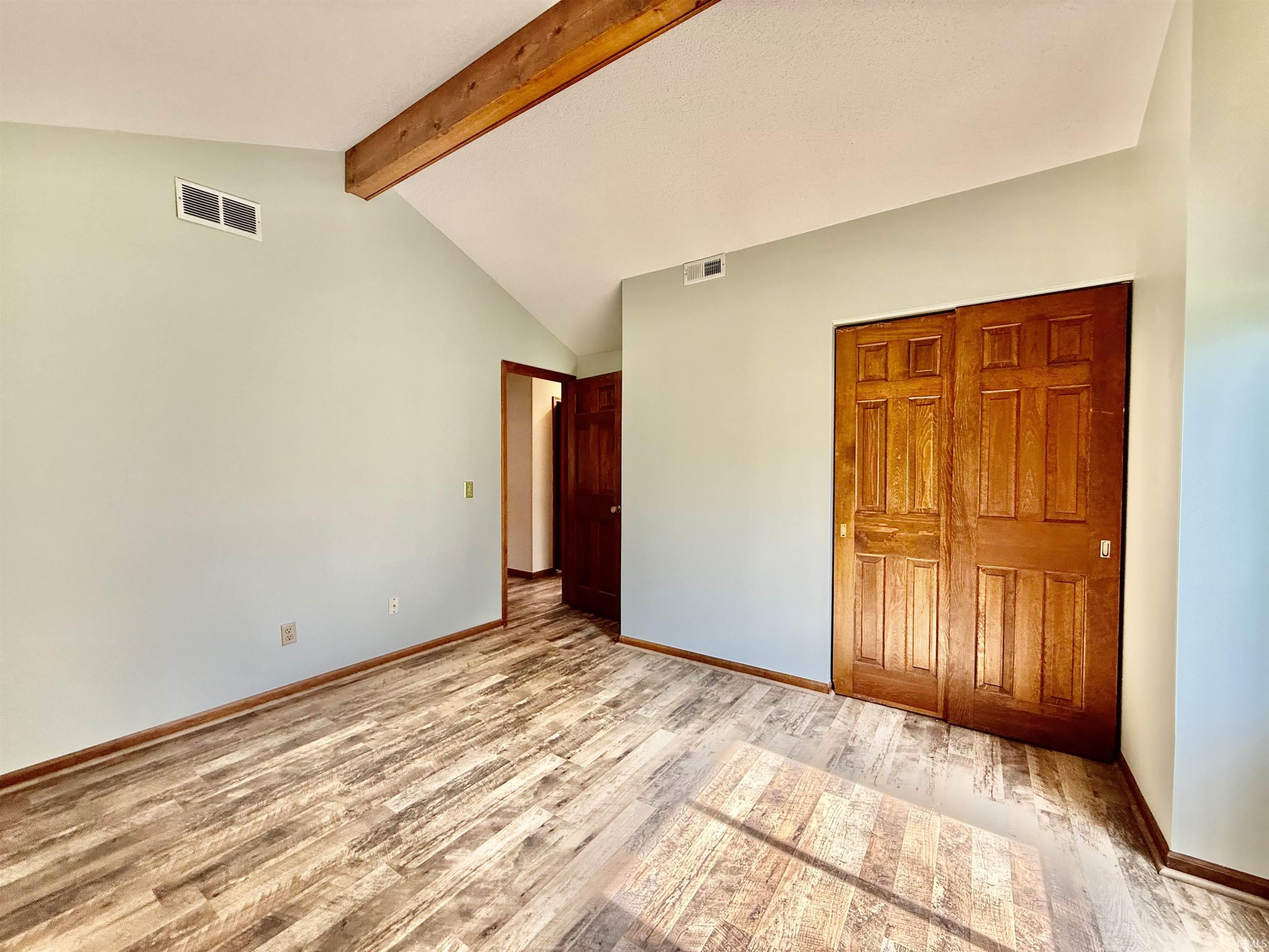Interior room featuring vaulted ceilings with an exposed wood beam, wood-finish flooring, and light green walls