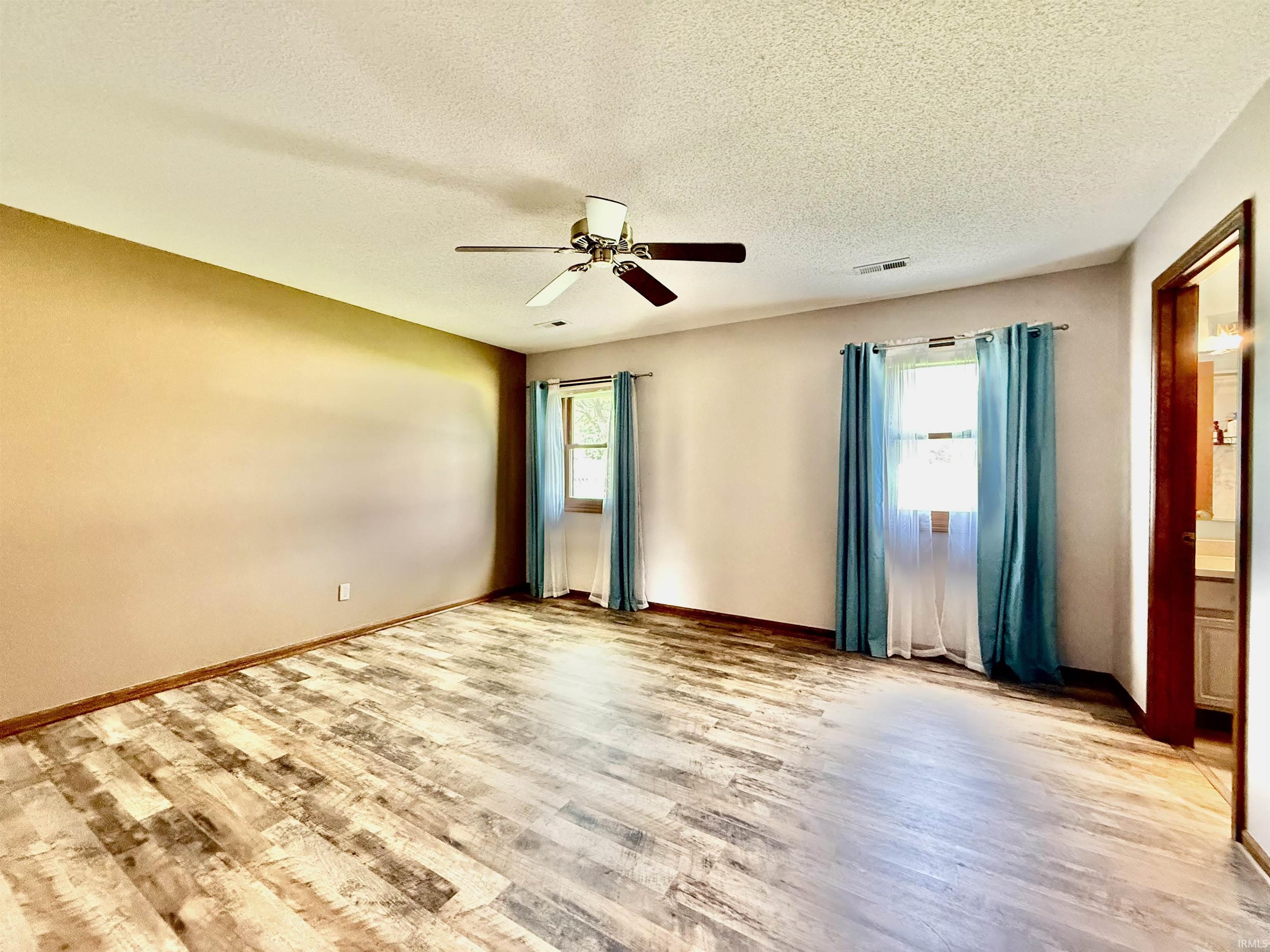 Spacious room featuring wood-finish flooring, two windows, and a ceiling fan