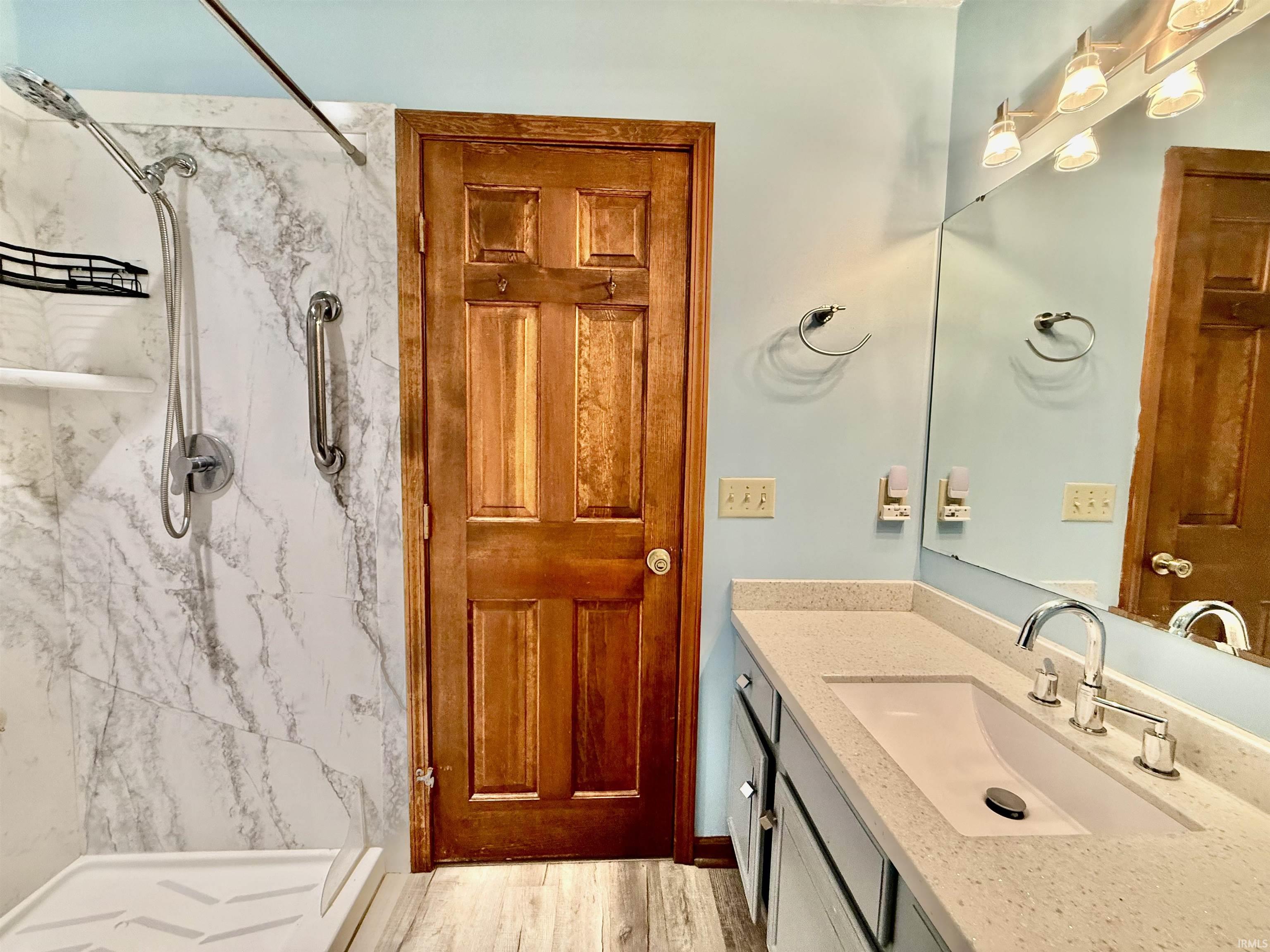 Bathroom featuring a walk-in shower with marble-look paneling, a grab bar, and a handheld showerhead