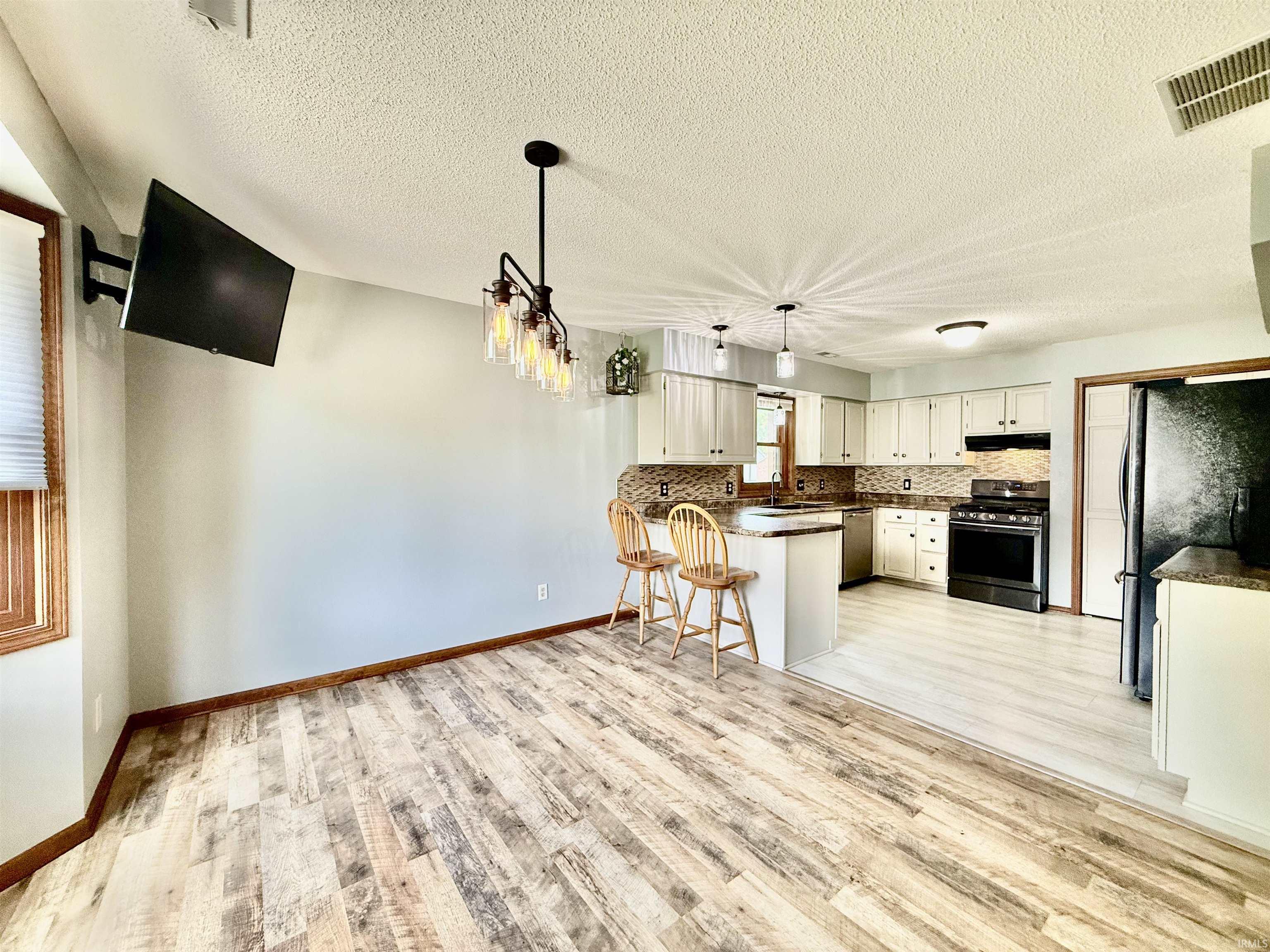 Spacious eat-in kitchen area featuring wood-finish flooring, a contemporary chandelier, and a breakfast bar