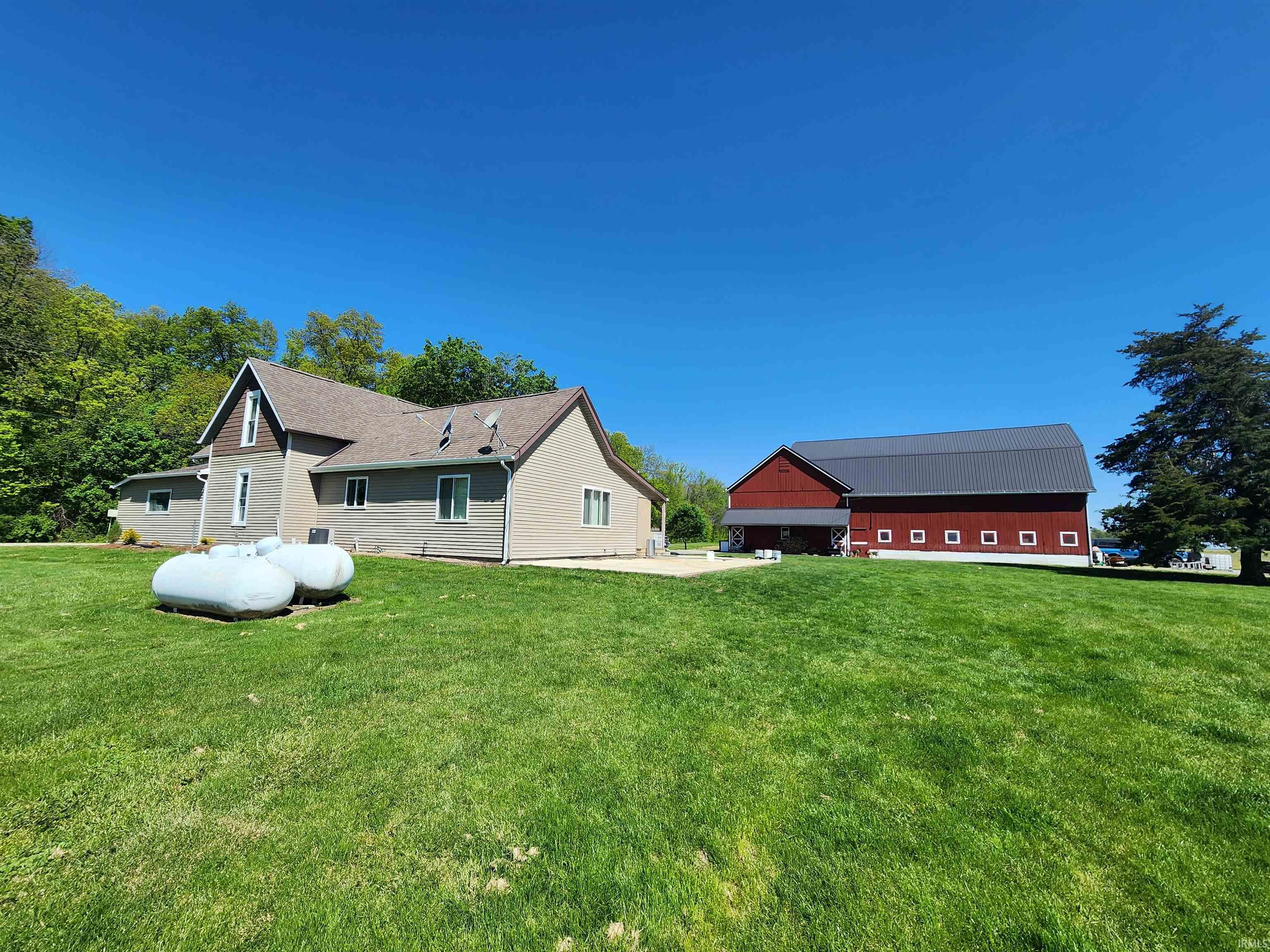 Spacious property featuring a primary residence with tan siding, a brown shingle roof, and an expansive green lawn