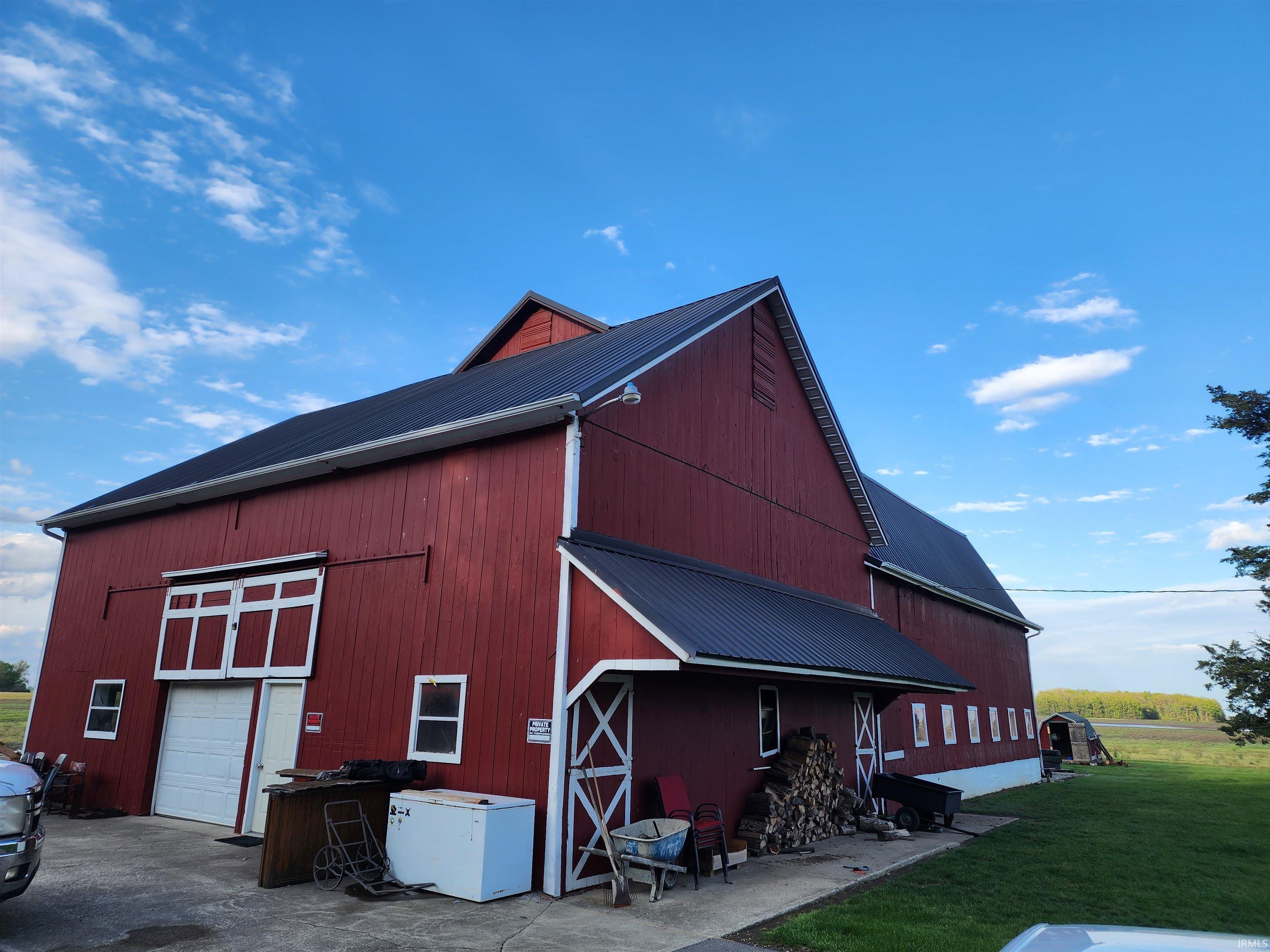 Red-sided barn structure featuring a dark metal roof, white trim accents, and a large garage door