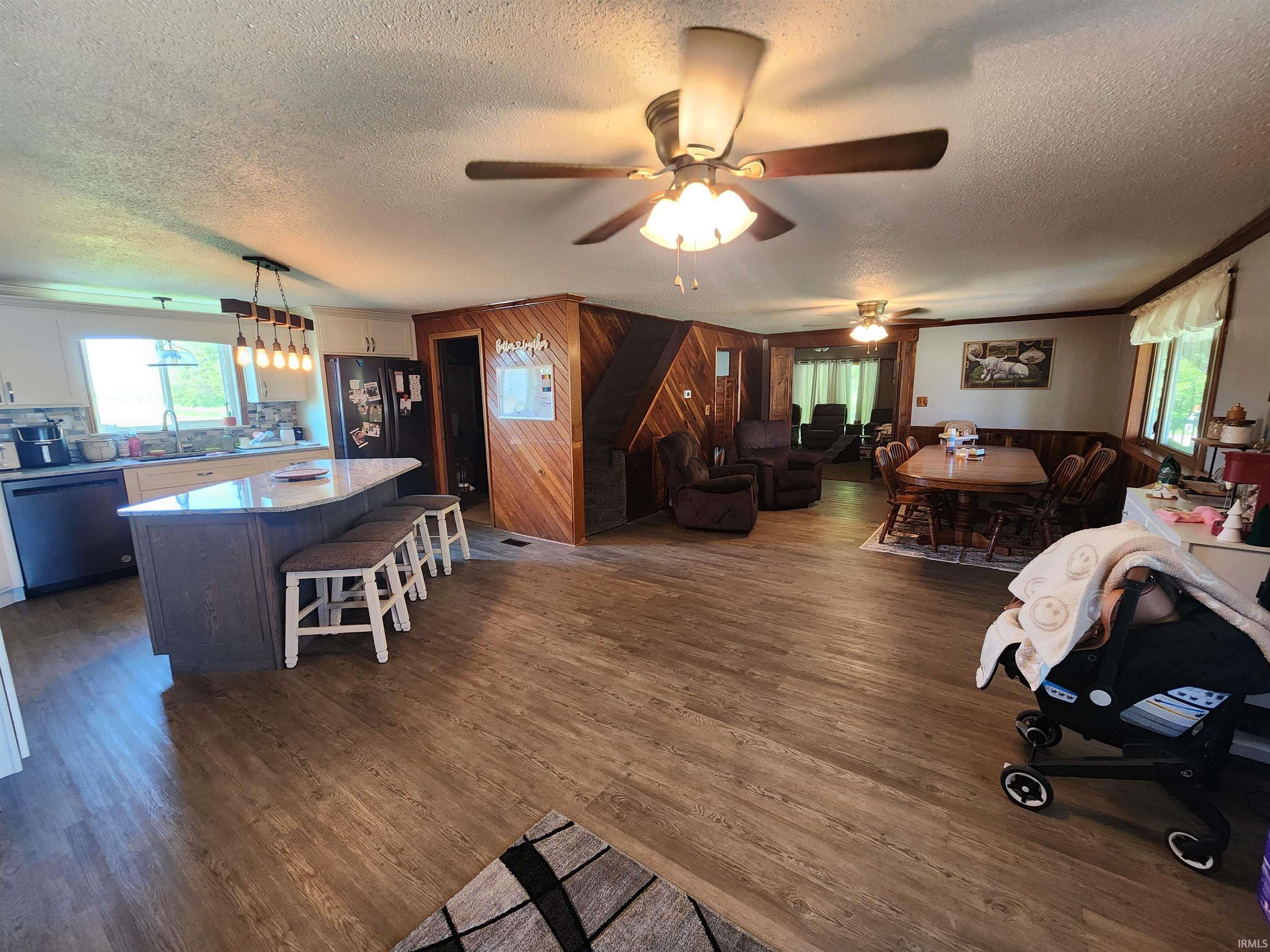 Open-concept living area featuring wood-finish flooring, a kitchen island with seating, a modern pendant light fixture, and two ceiling fans