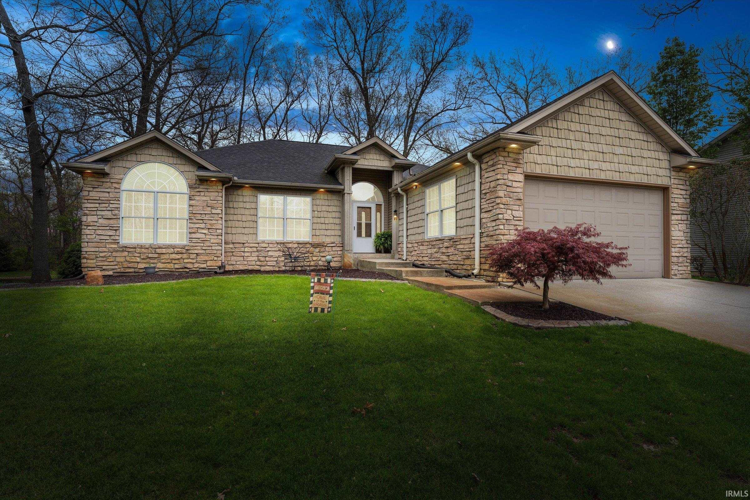 Stone and shake-sided ranch-style home featuring a prominent two-car garage, arched window, and landscaped front yard