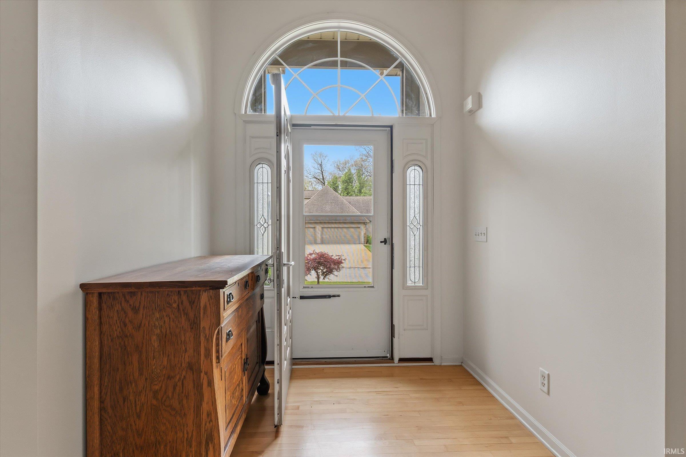Entryway featuring a white door with an arched transom window, sidelight windows, and wood-finish flooring
