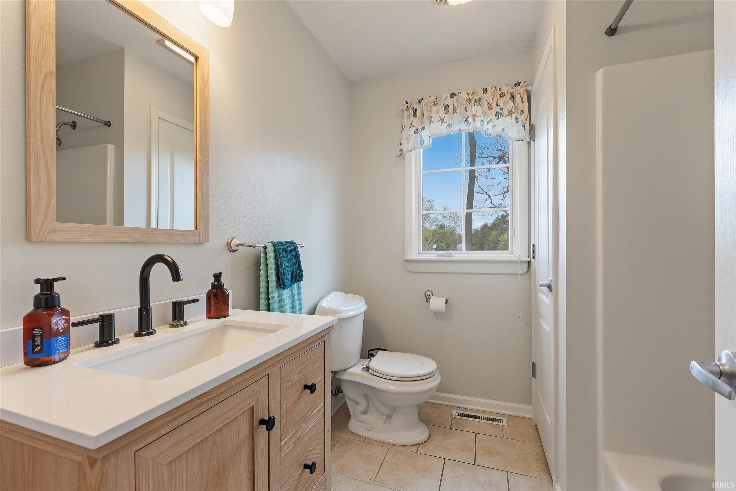 Bathroom featuring a light wood-finish vanity with a white countertop and rectangular sink, matte black faucet, and a framed mirror