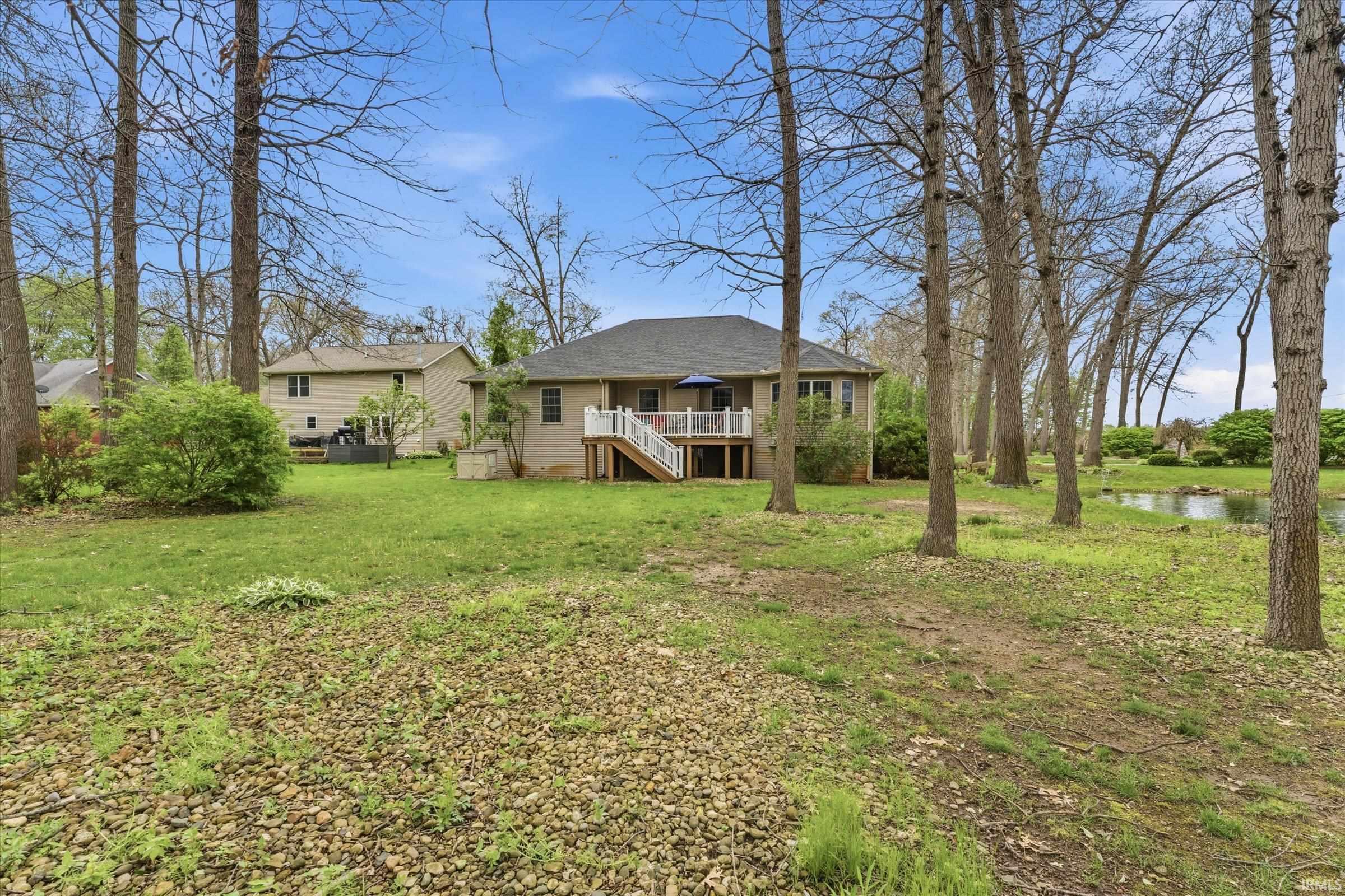 Expansive backyard featuring mature trees, green lawn space, and a visible pond