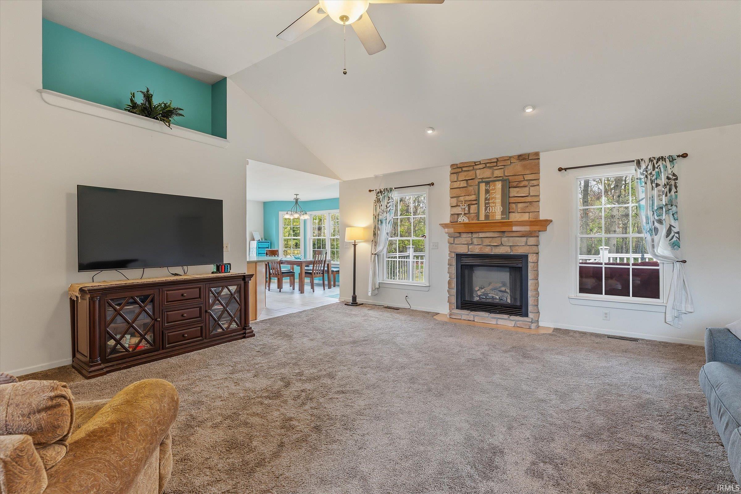 Spacious living area featuring a vaulted ceiling with a ceiling fan, a stone-faced fireplace with a wooden mantel, and recessed lighting