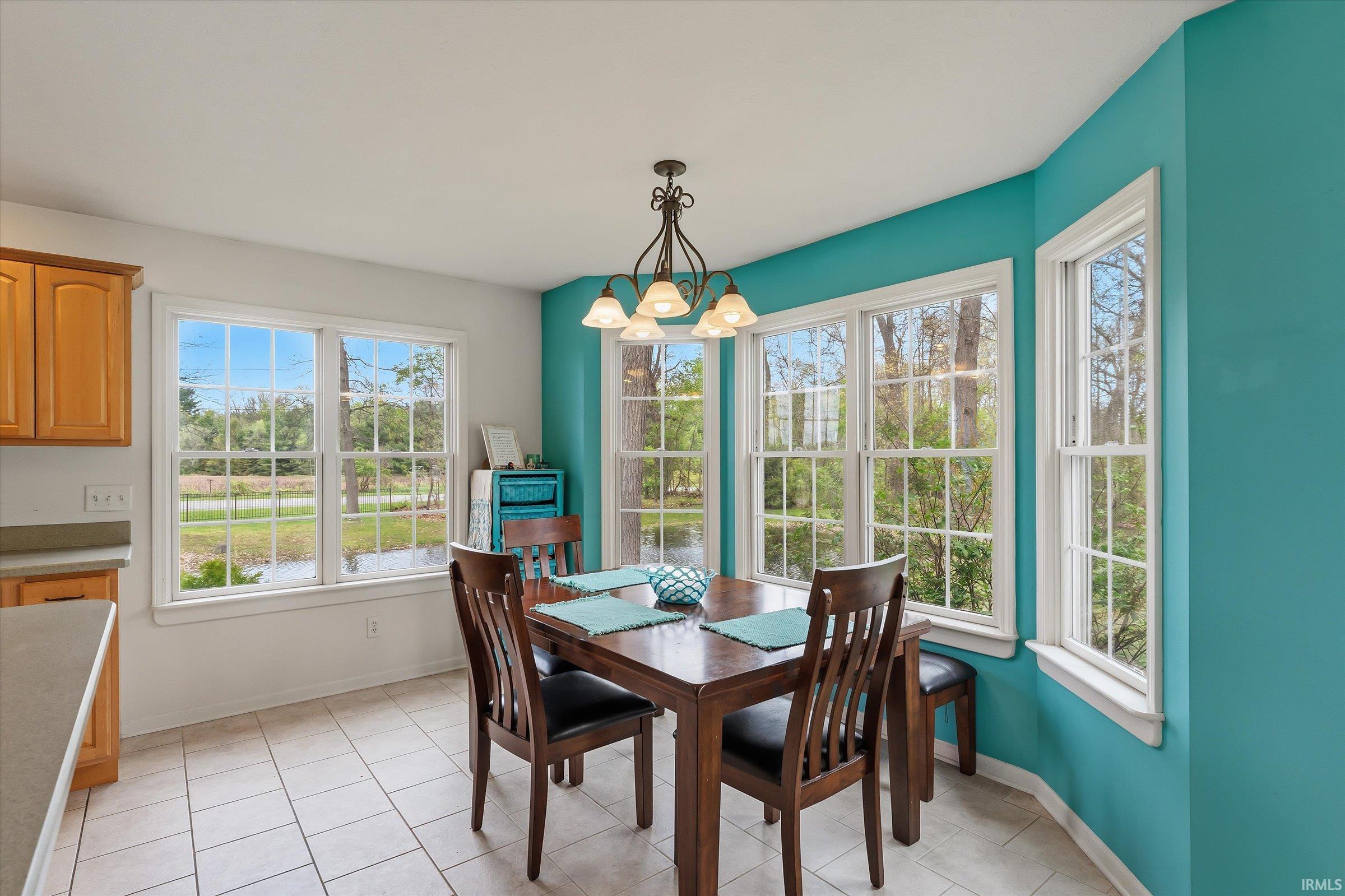 Dining area featuring extensive fenestration, ceramic tile flooring, a multi-light chandelier, and a built-in breakfast bar with a light wood-finish cabinet and solid surface countertop