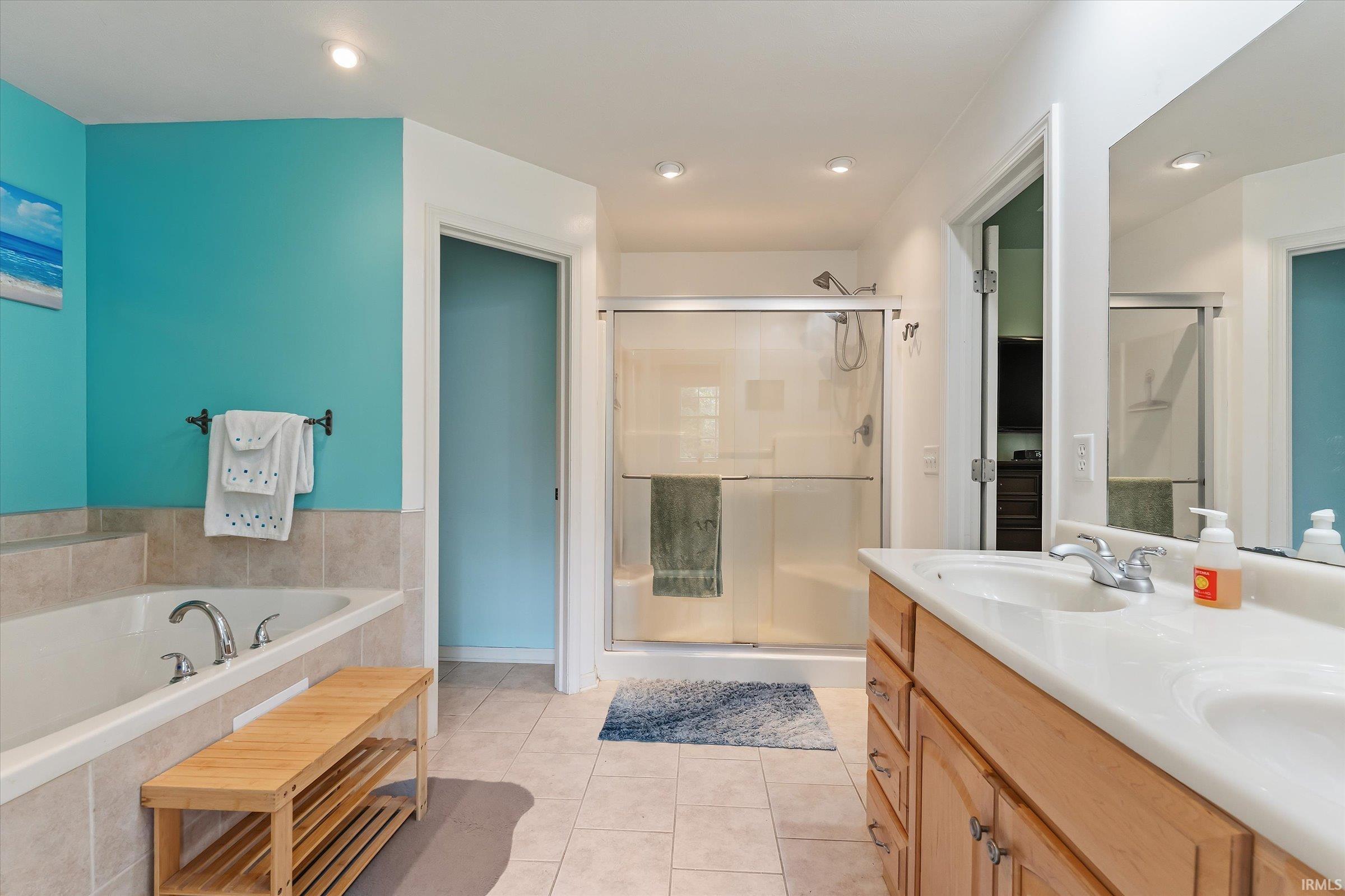 Bathroom featuring a built-in soaking tub with tile surround, a glass-enclosed shower, dual vanity with integrated sinks, and recessed lighting