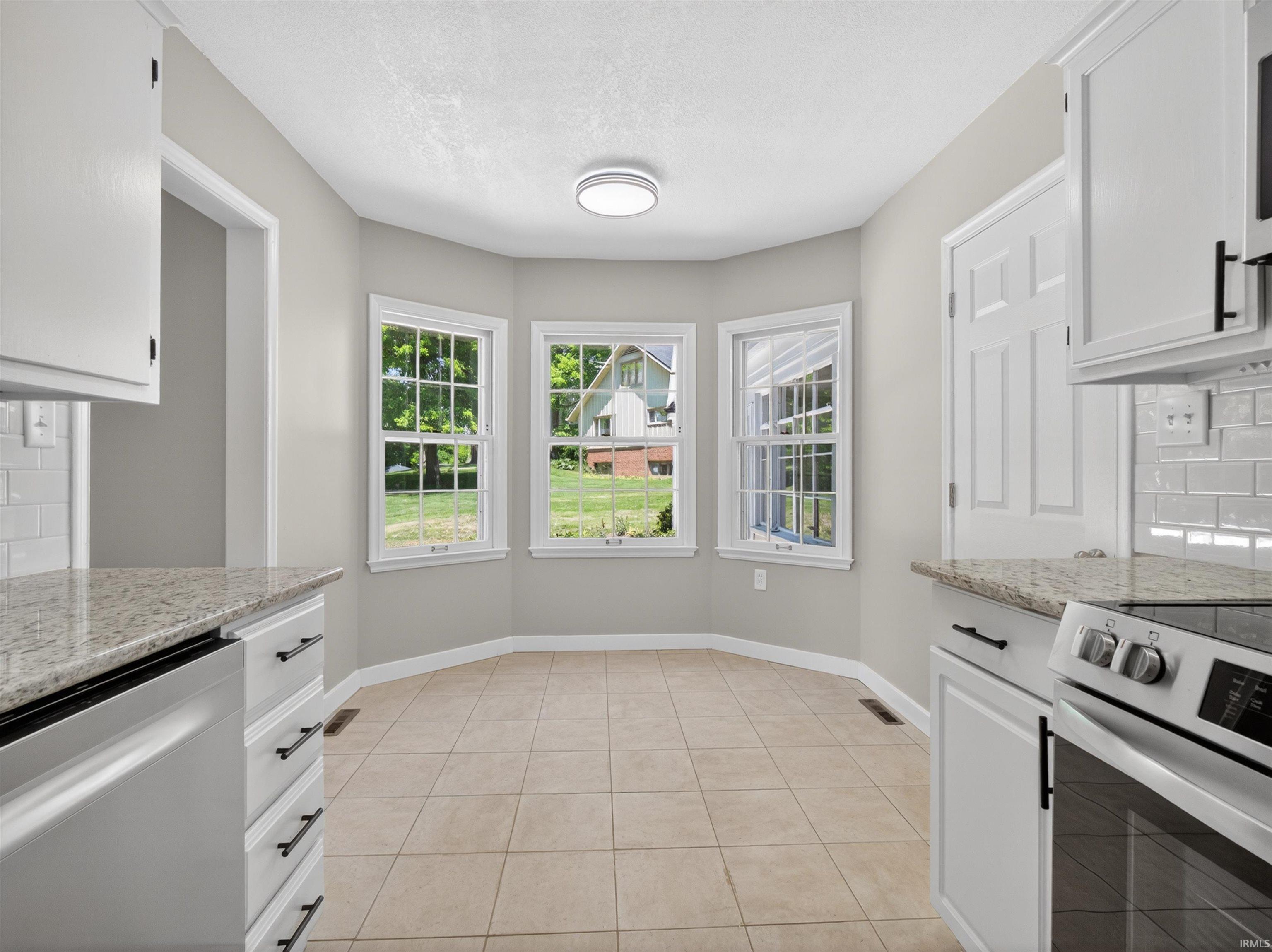 Kitchen dining area featuring a three-panel bay window, light tile flooring, white cabinetry, and granite countertops