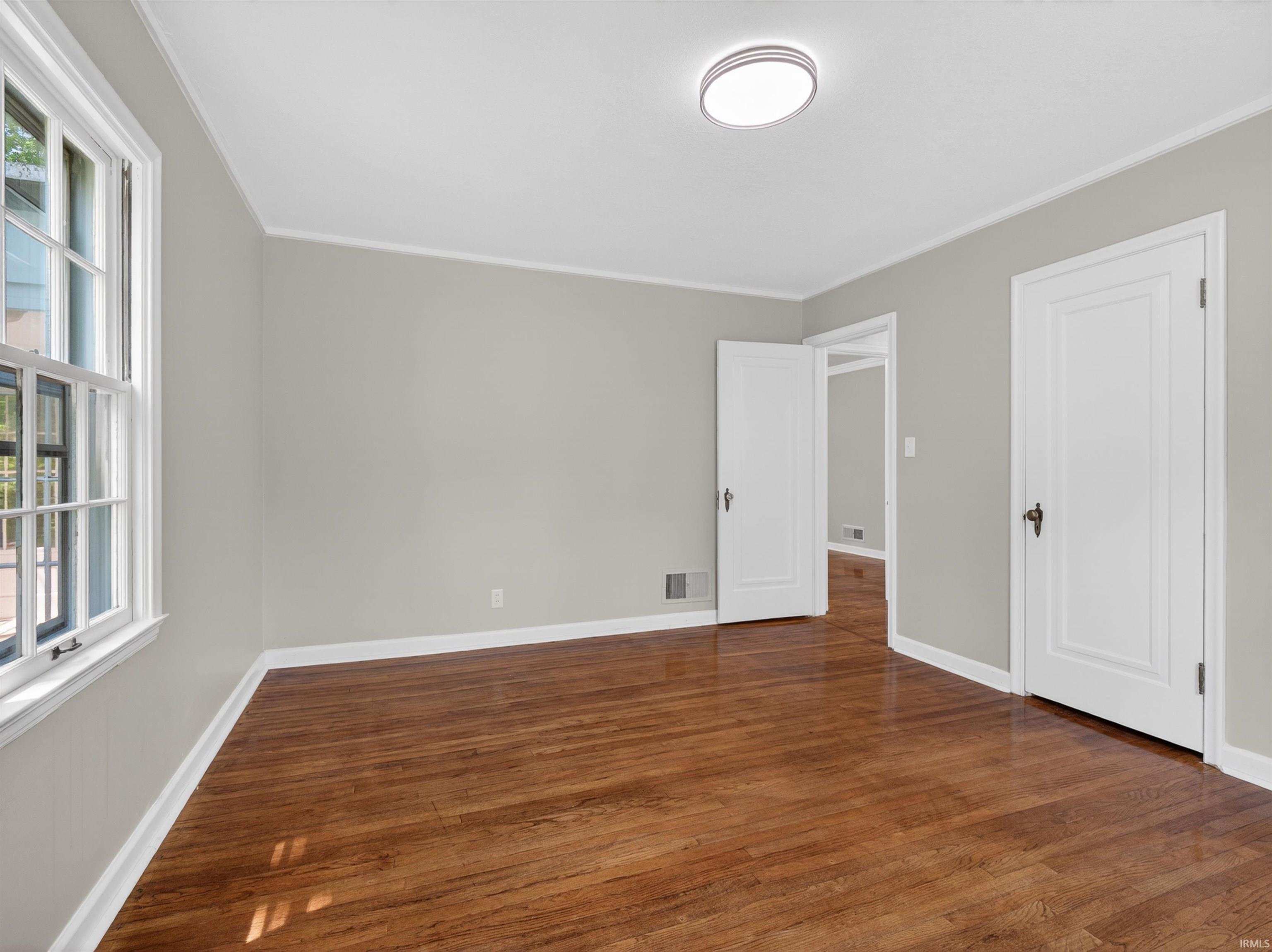 Hardwood flooring extends throughout this room, featuring light gray walls, white trim, and a ceiling-mounted light fixture