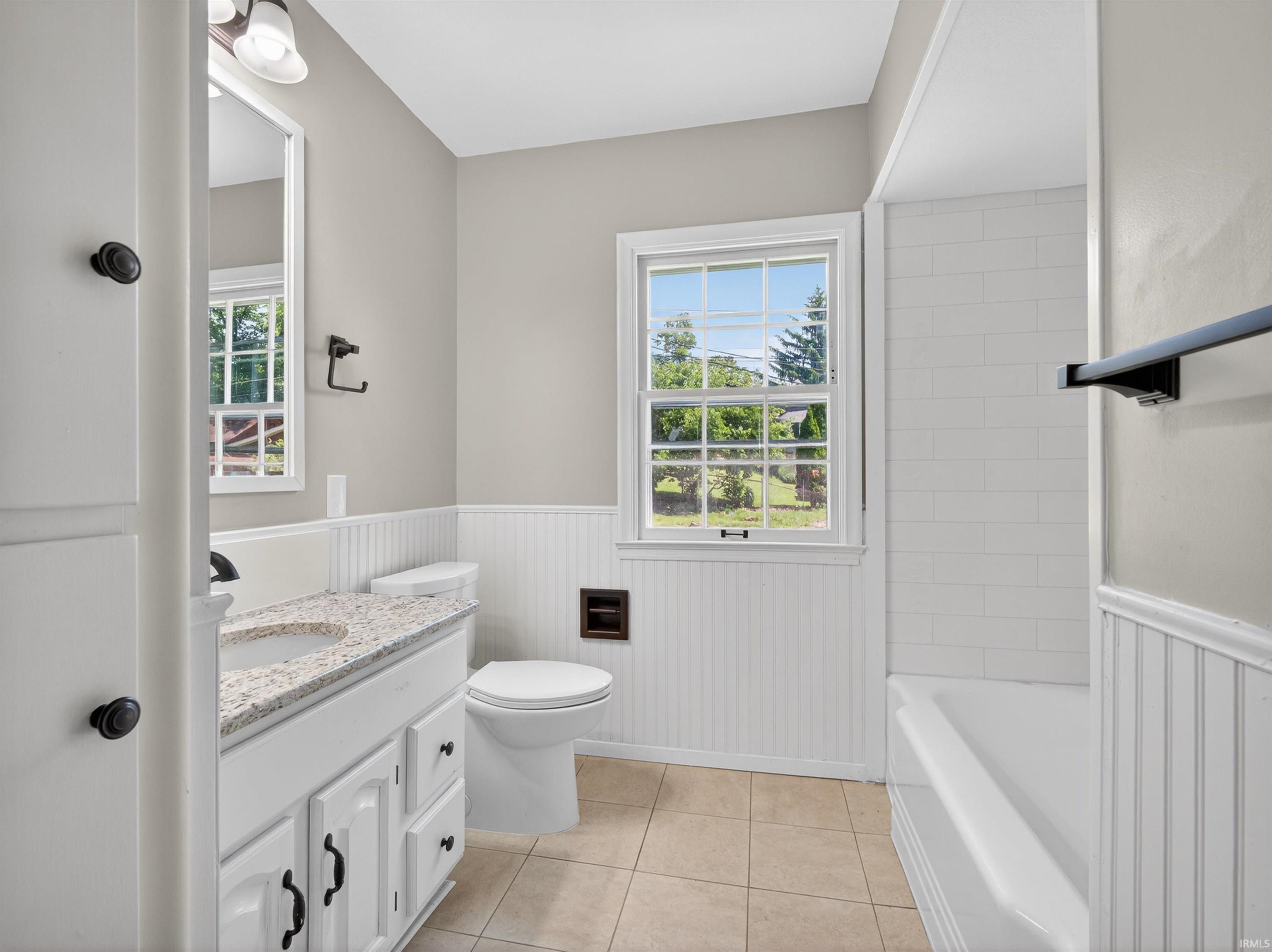 Bathroom featuring a white vanity with a light-toned granite-style countertop, a white toilet, and a white tub with subway tile surround